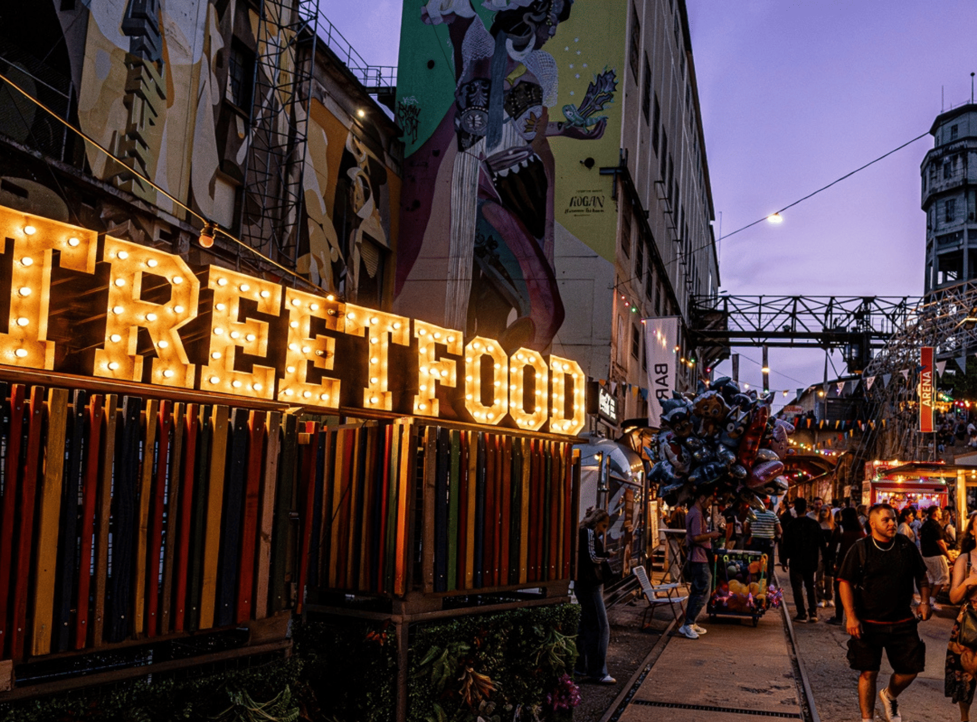 Besucher schlendern über ein Streetfood-Festival mit bunten Foodtrucks, Lichterketten und Essensständen aus aller Welt.