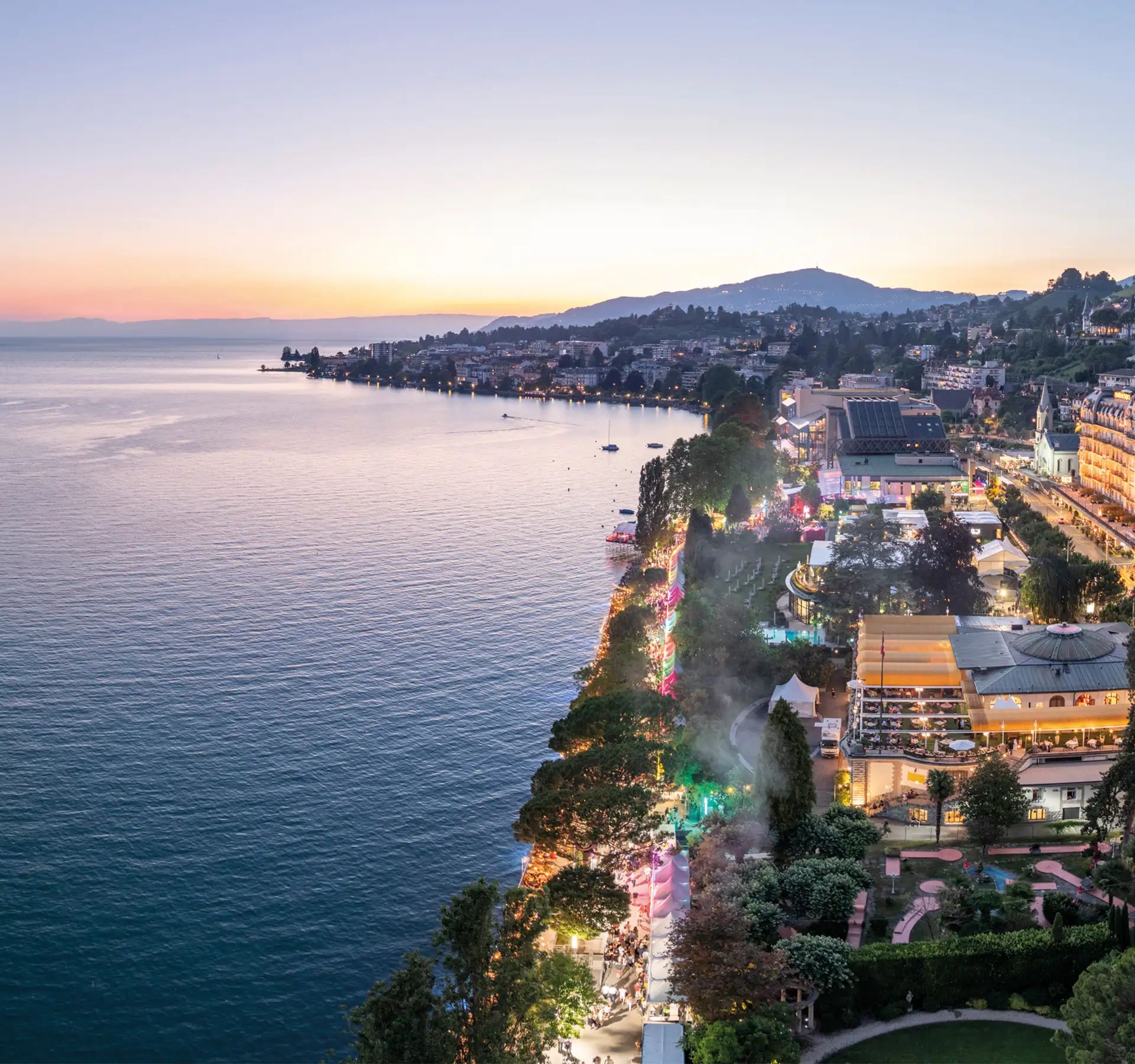 Vue sur la promenade du bord du lac Léman à Montreux au coucher du soleil avec des bâtiments éclairés et des montagnes en arrière-plan