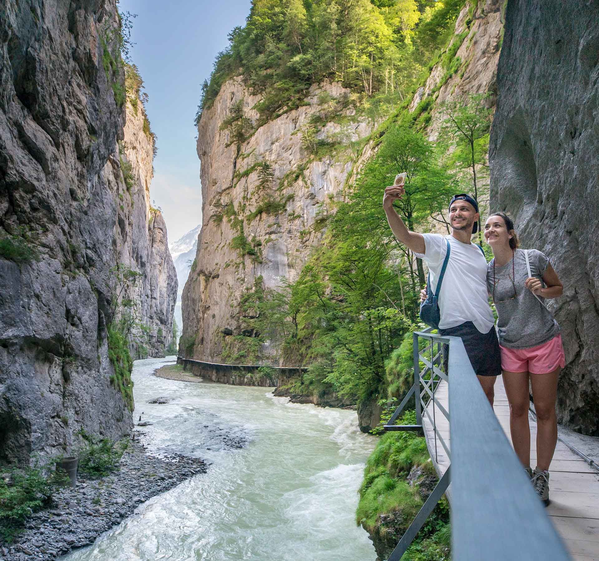 Due persone fanno un selfie su una passerella stretta nella gola dell'Aare con pareti rocciose ripide e un fiume.