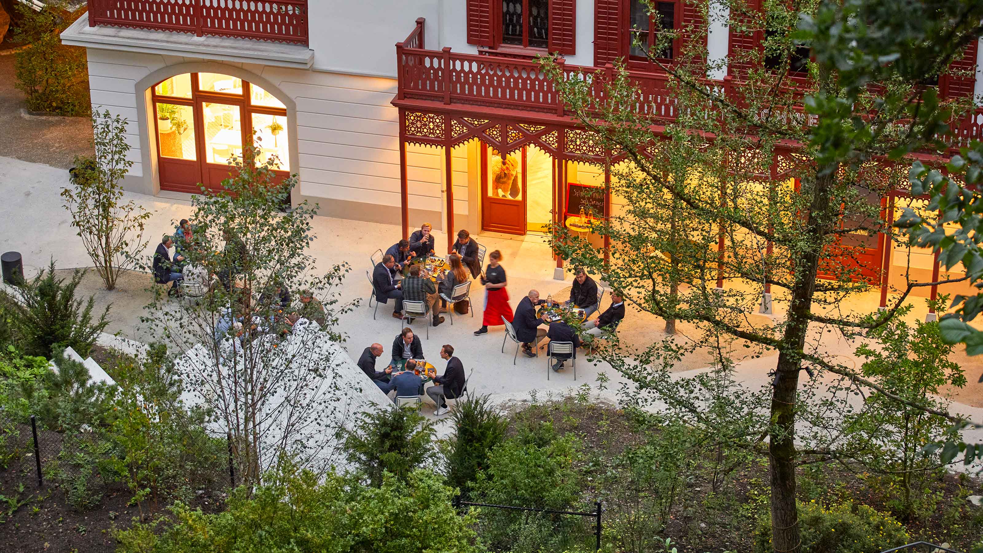 Un gruppo variopinto di persone siede ai tavoli di fronte a un edificio e prende un aperitivo.
