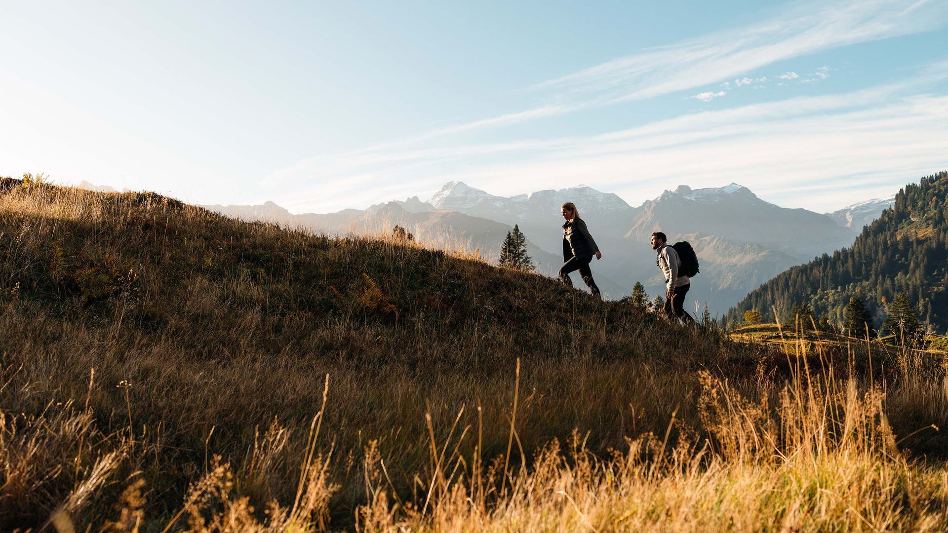 Ein Mann und eine Frau erklimmen einen Hügel mit spektakulärem Panorama auf die Berge.