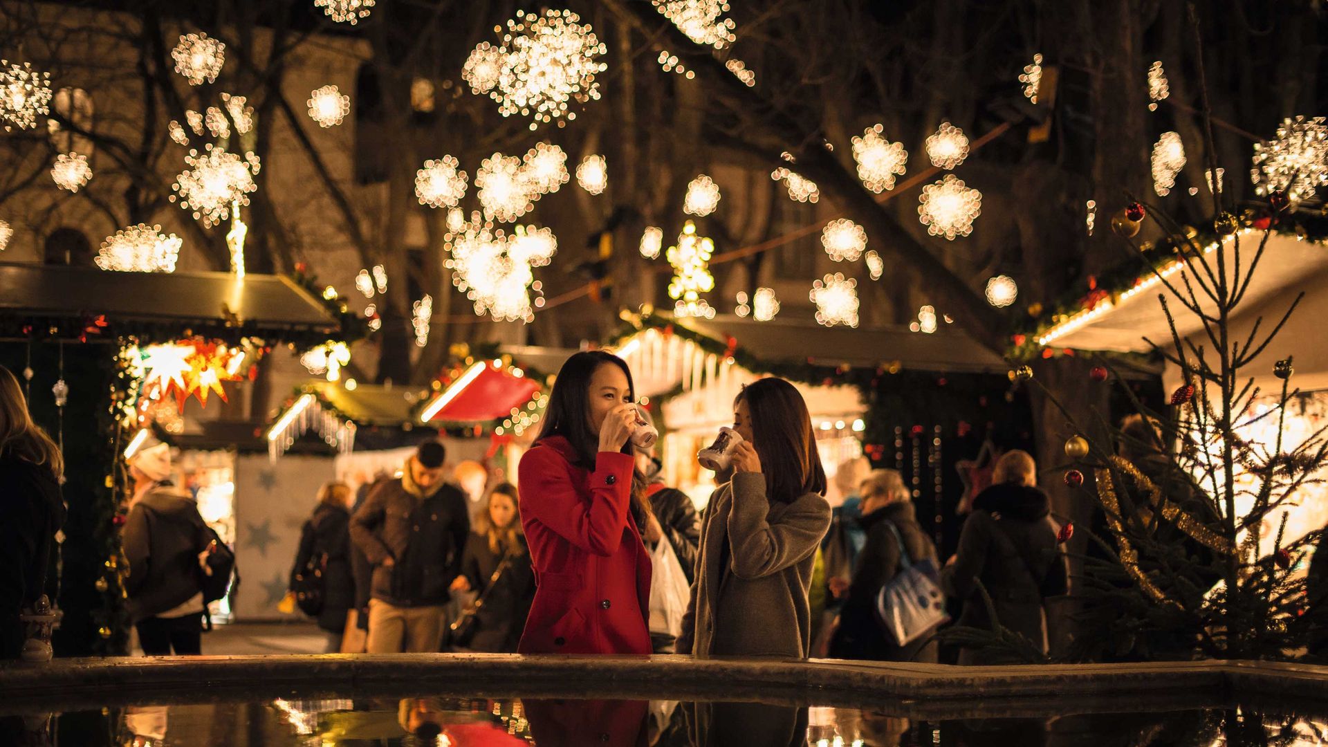 A woman stands by a fountain at night, illuminated by soft lights, creating a serene and peaceful atmosphere.