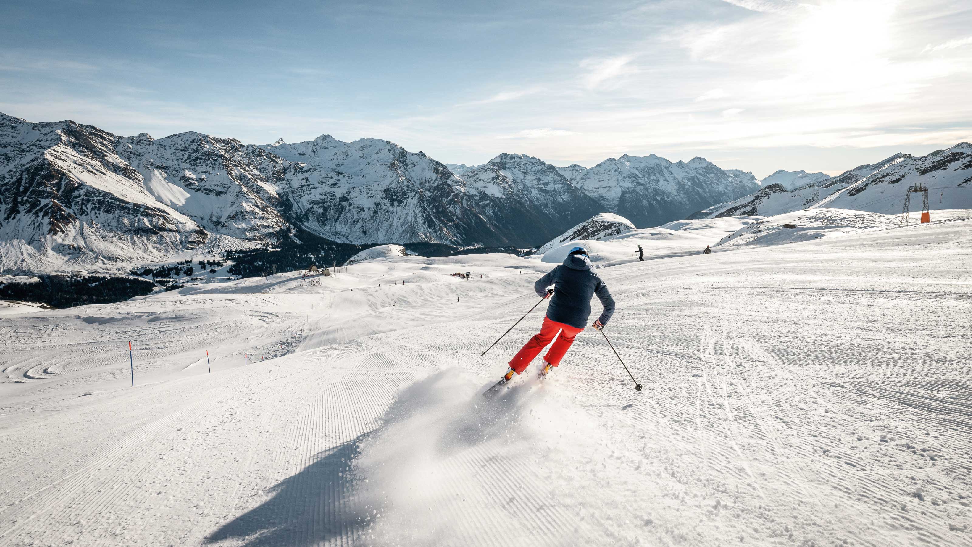 Uno sciatore scende lungo una pista battuta davanti a un panorama montano mozzafiato.