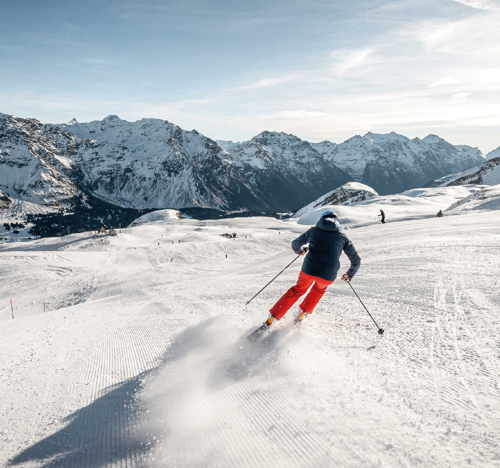 A skier descends a groomed slope against an impressive mountain backdrop.