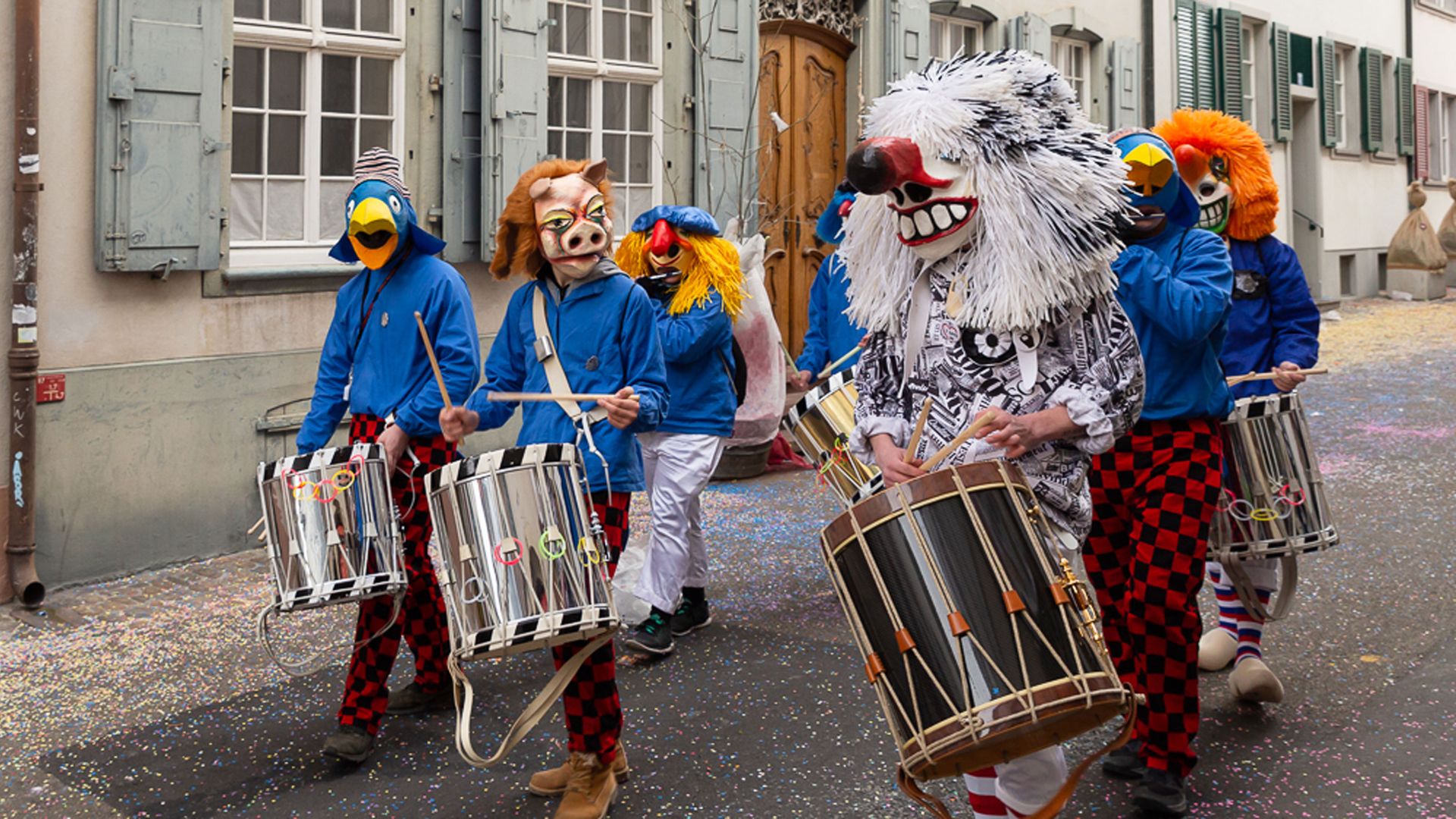 People in colorful masks parading through the streets of Basel during carnival.