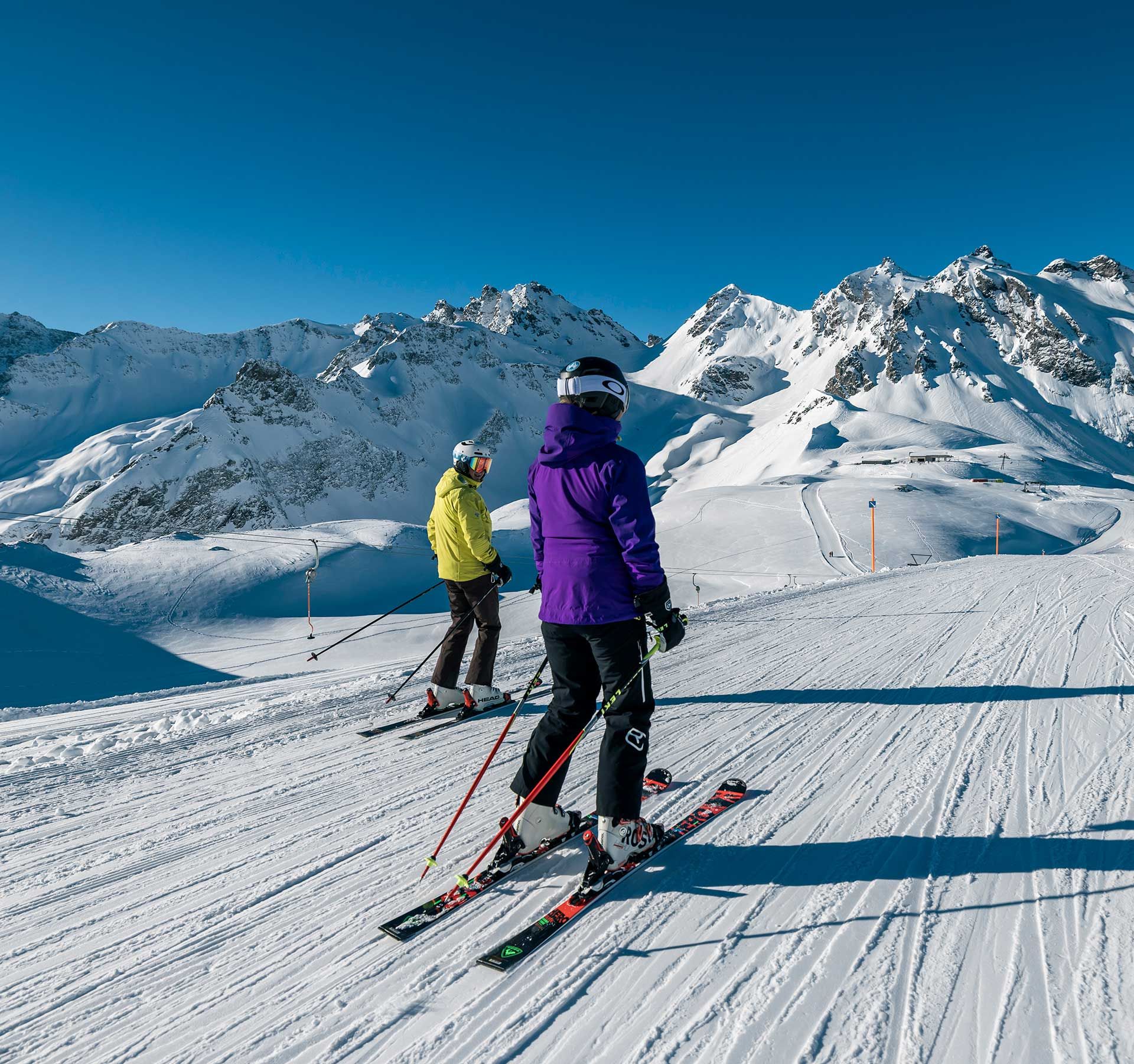 Zwei Skifahrer fahren durch eine verschneite Gebirgslandschaft und zeigen ihr Können vor einer Kulisse aus unberührtem weißen Schnee.