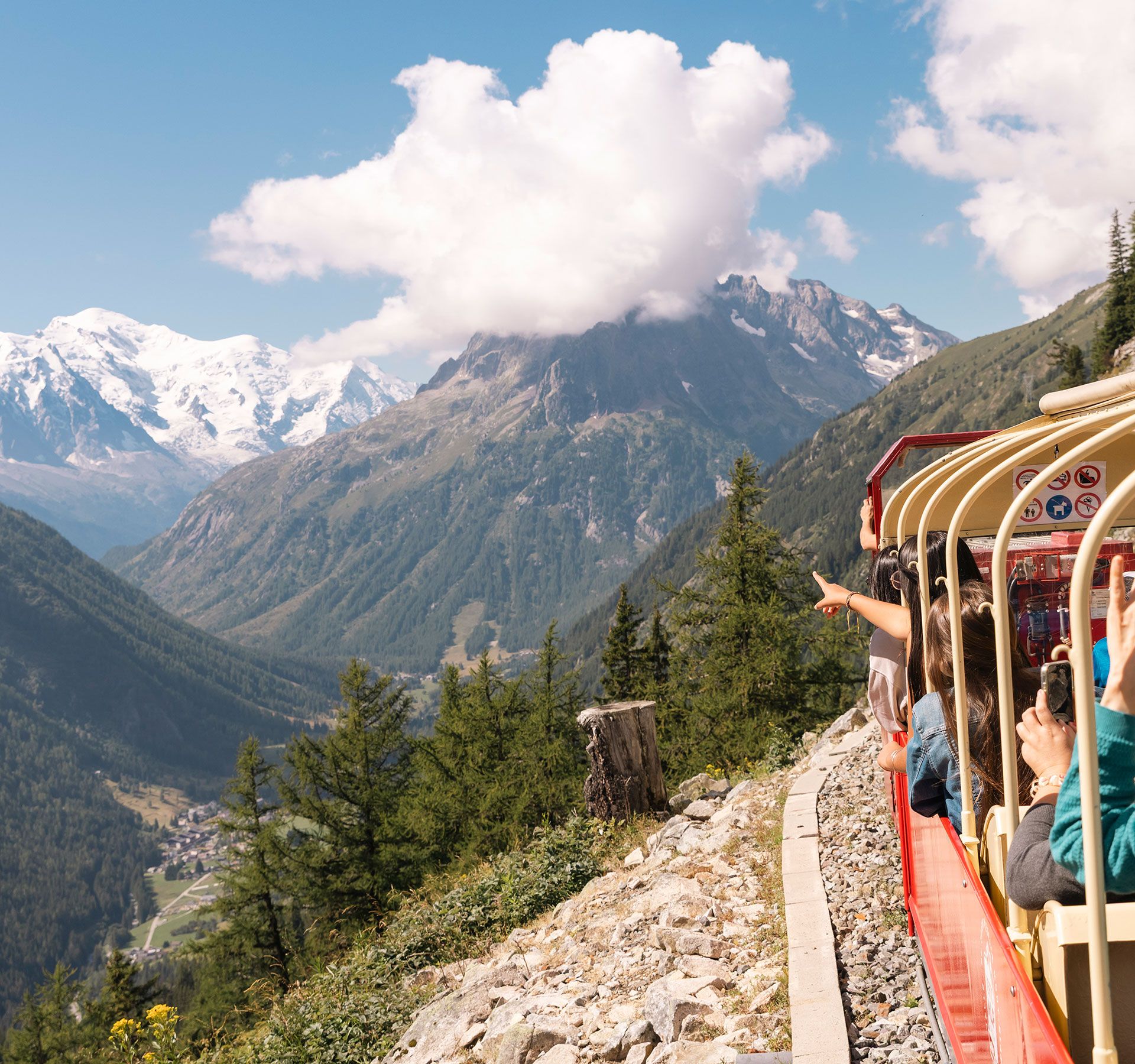 Un train rouge se déplace à travers les montagnes sur une route sinueuse.
