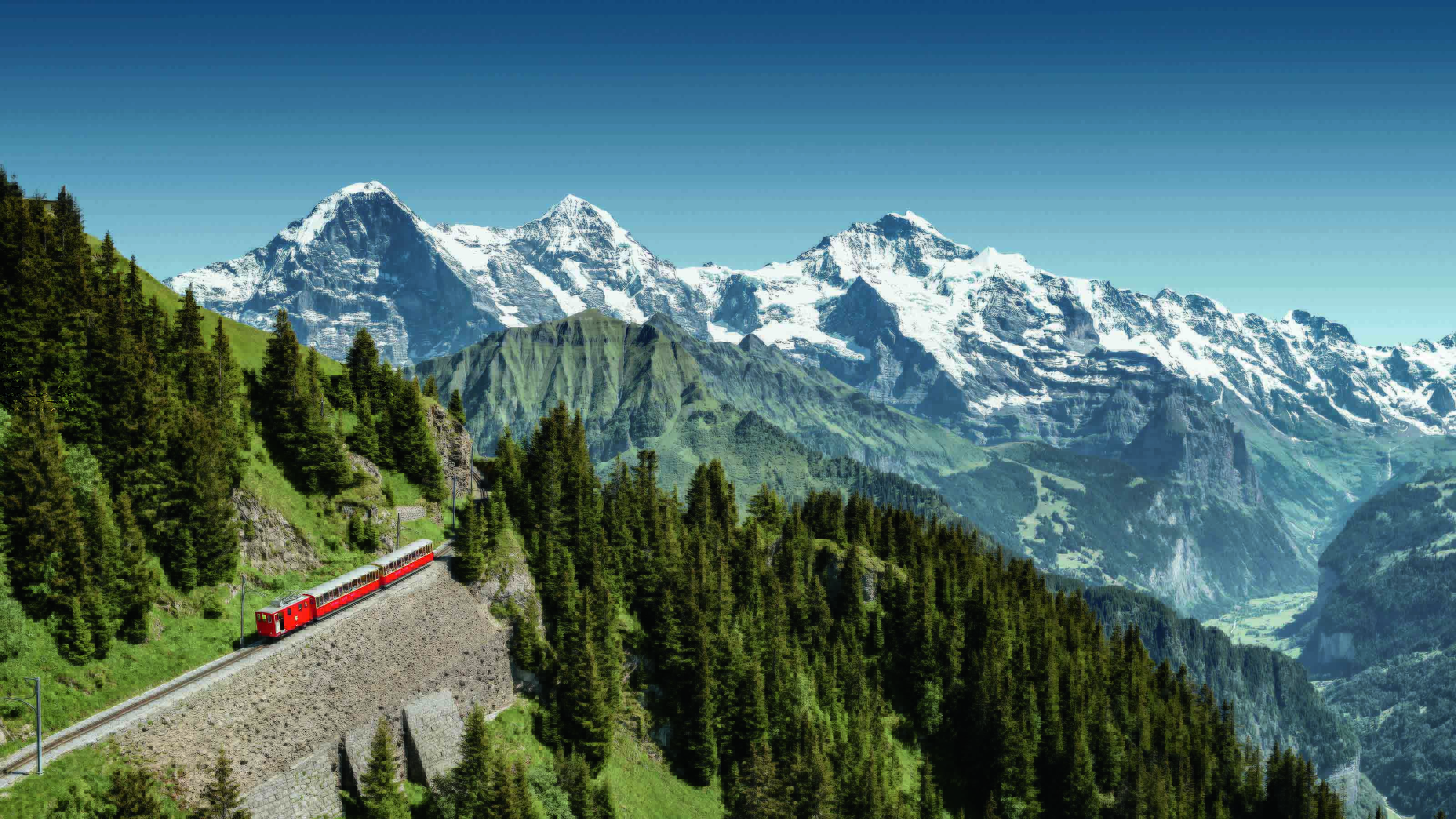 Aerial view of the cogwheel going up the mountain. In the background, snow-covered peaks of the Eiger, Mönch and Jungfrau can be seen.