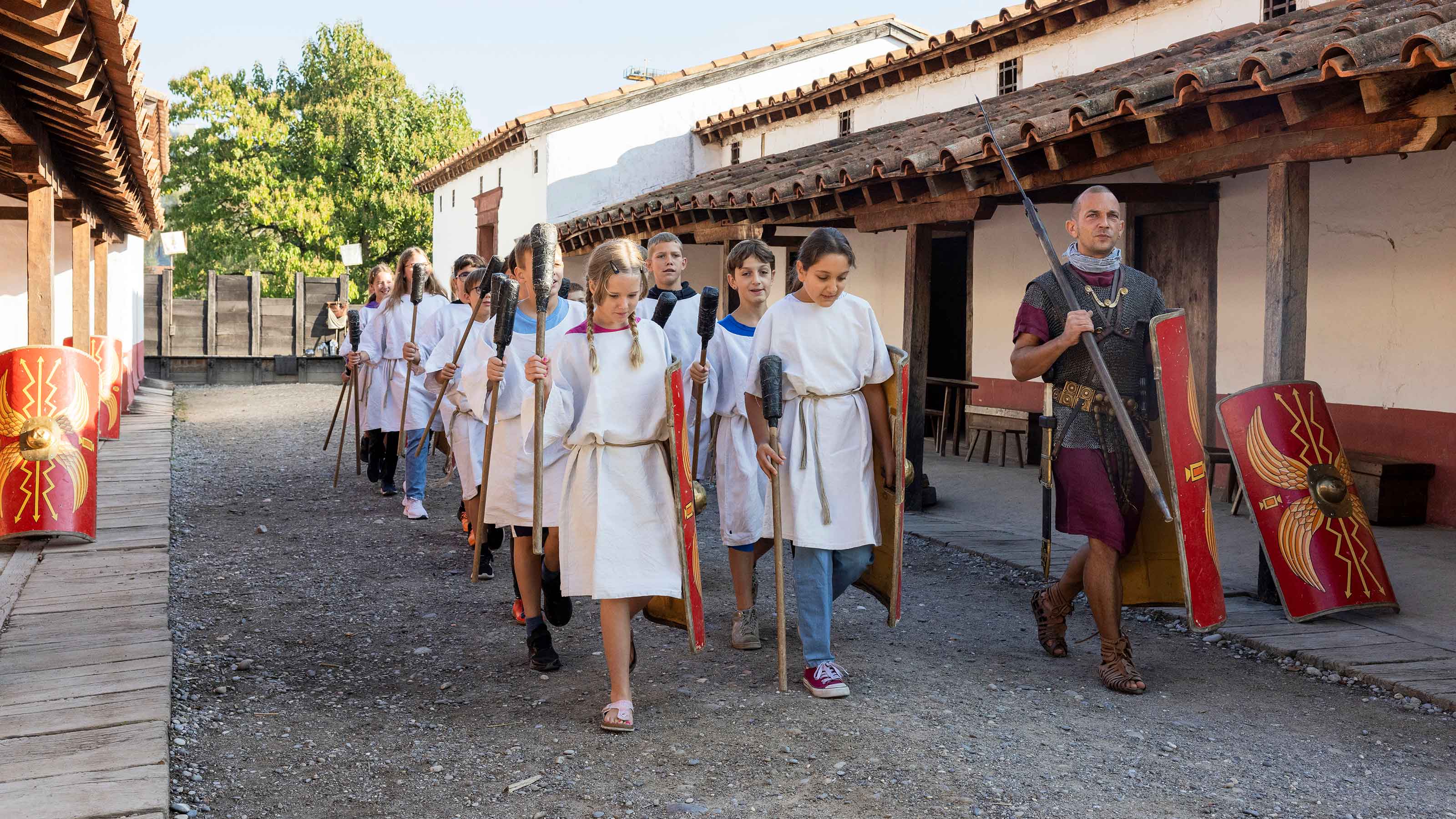 Eine Schulklasse in traditioneller römischer Kleidung geht eine belebte Straße entlang, die Geschichte und Kultur verkörpert.