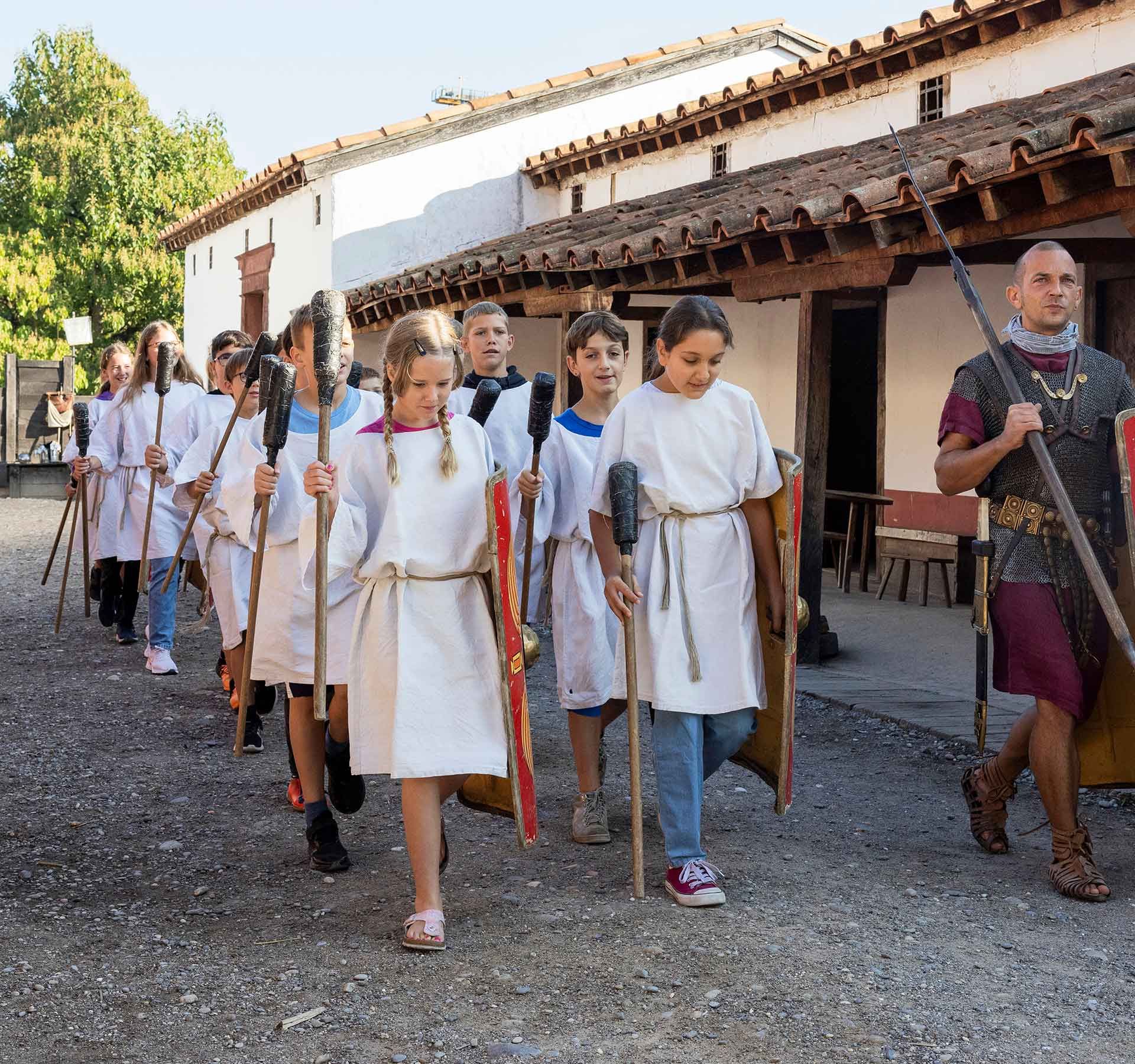 Una scolaresca in abiti tradizionali romani cammina lungo una strada trafficata che è sinonimo di storia e cultura.