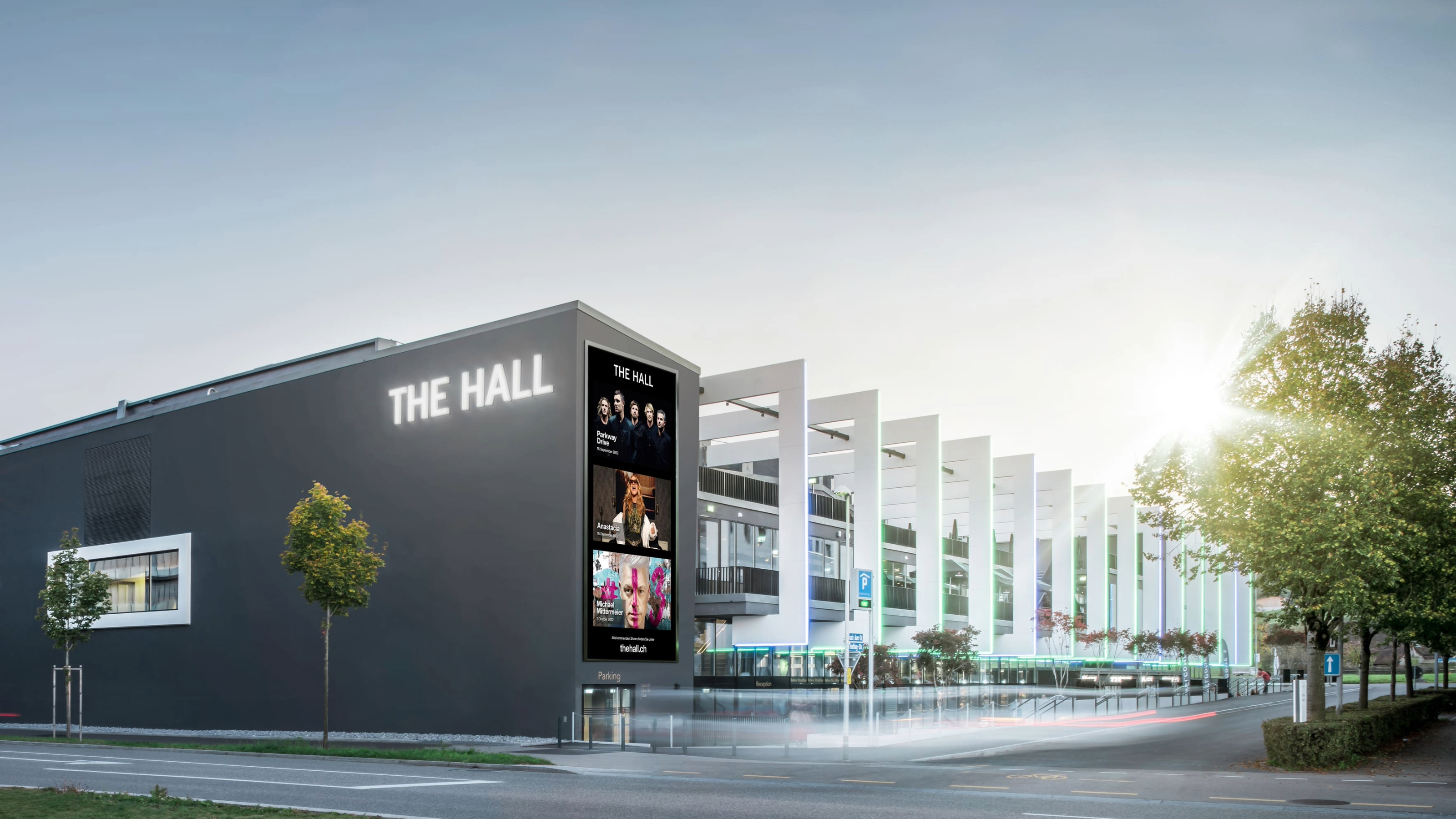 Modern event venue The Hall in Zurich, featuring a glass façade and bright evening lighting, surrounded by urban architecture.