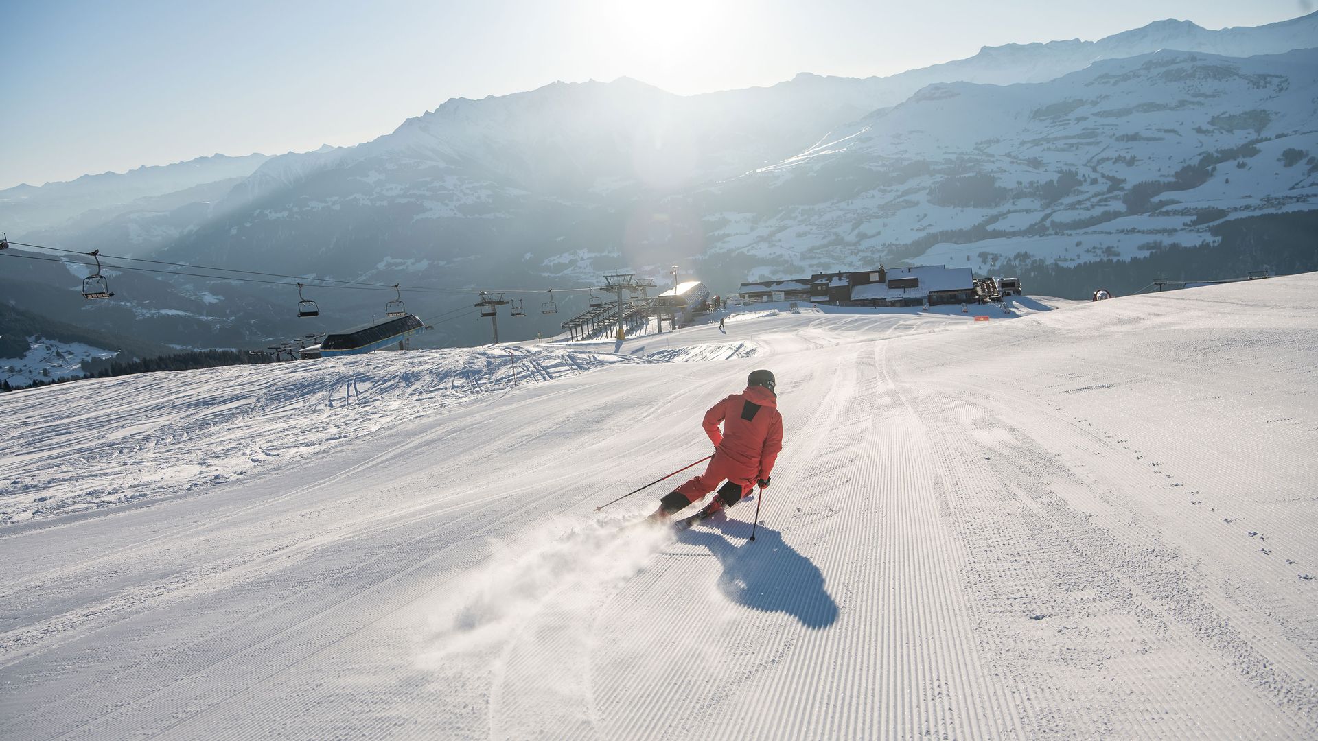 Ein Skifahrer fährt einen schneebedeckten Berg hinunter und zeigt vor einer atemberaubenden Bergkulisse sein Können und seine Geschwindigkeit.