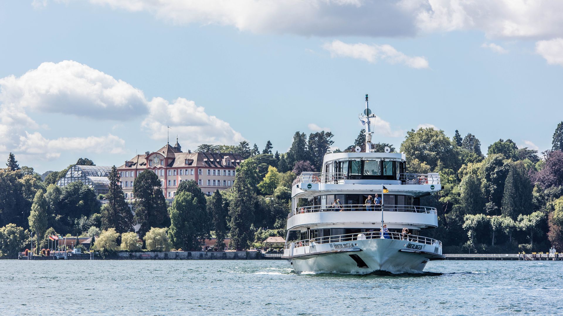 Ein Schiff mit Passagieren entfernt sich vom Ufer.