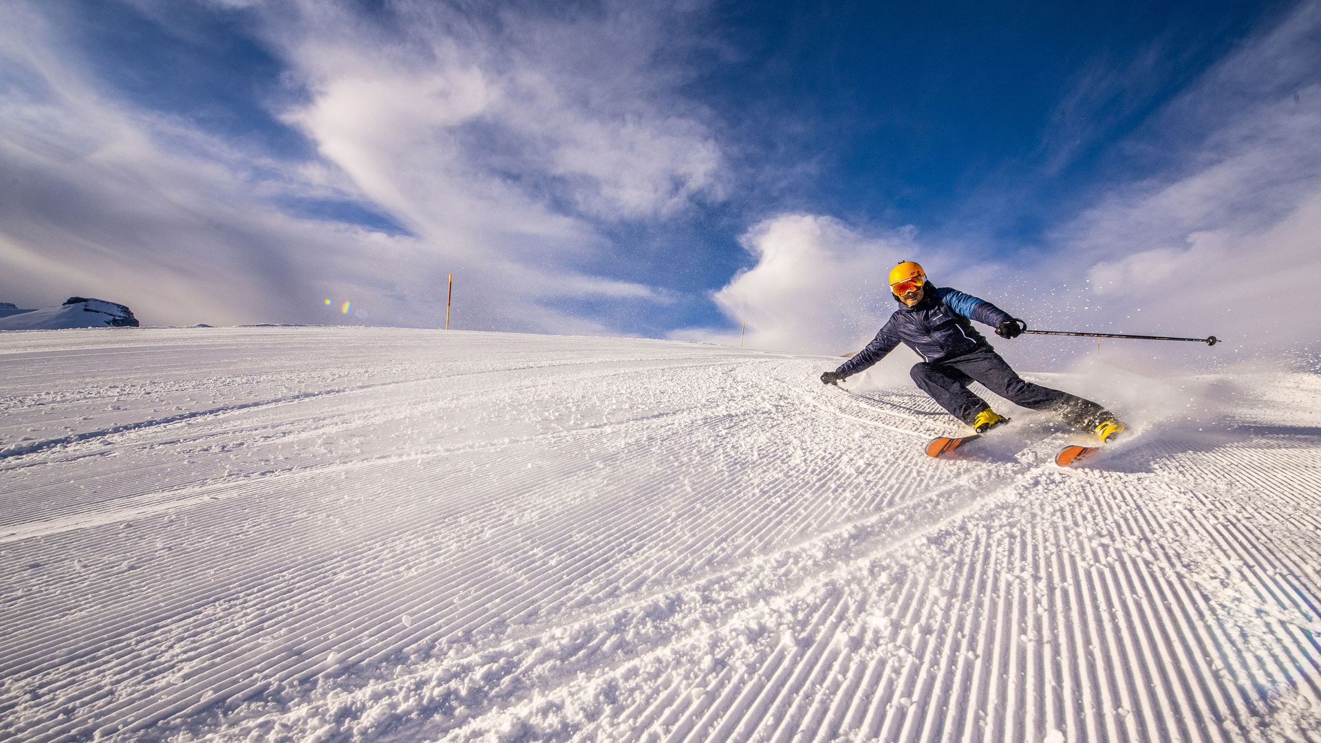 The picture shows a skier on a freshly groomed slope. He is leaning steeply into the turn and the snow is swirling up behind him. 