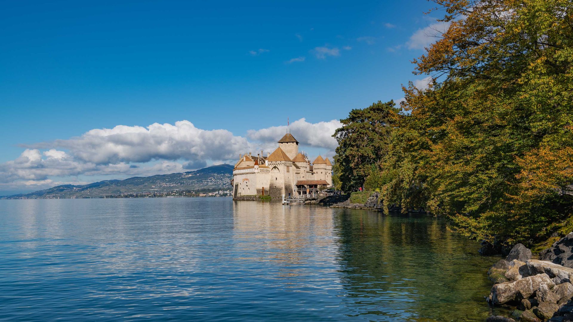 Schloss am Seeufer mit Bergen im Hintergrund