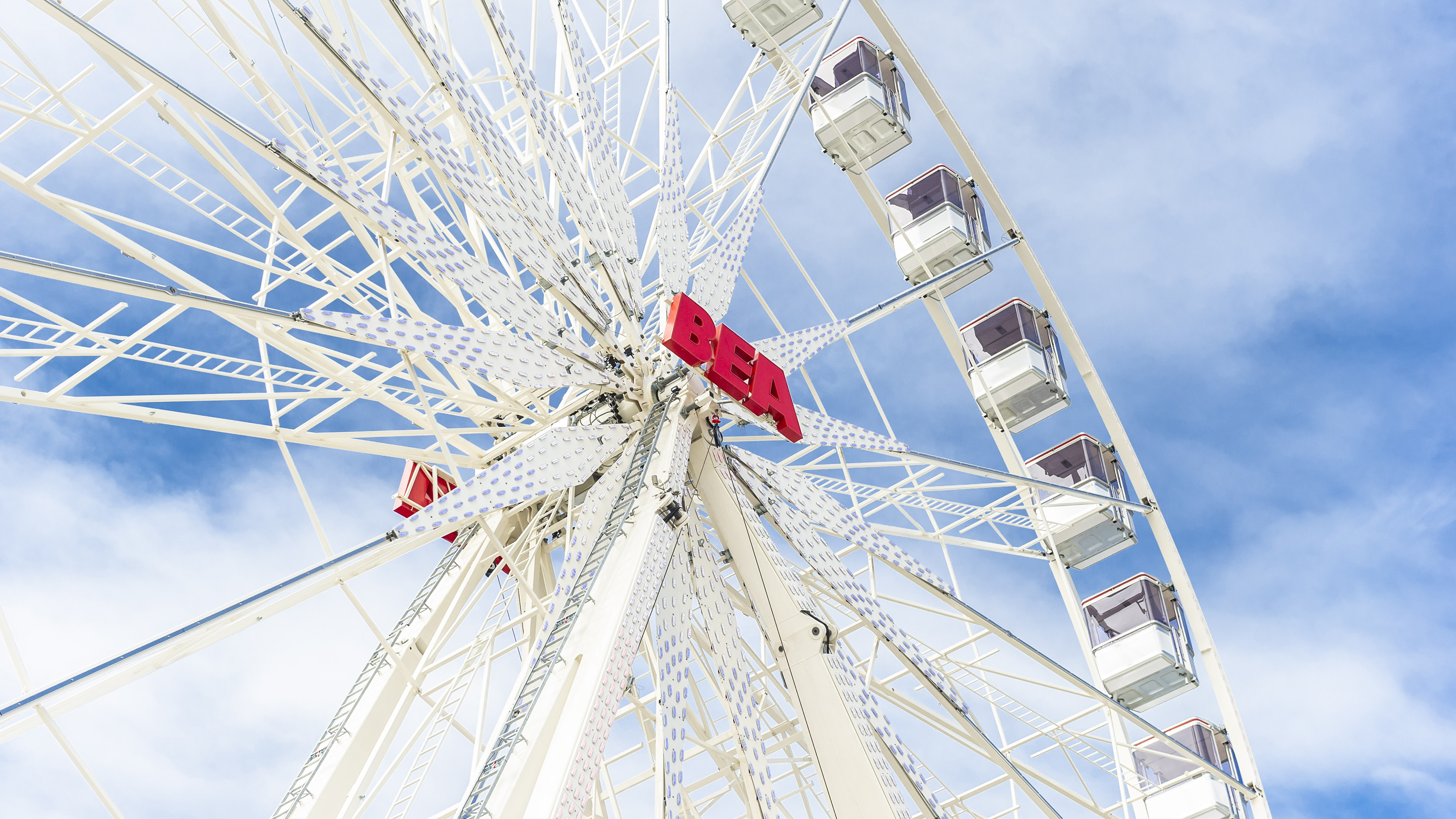 Ferris wheel at the BEA fair in Bern with colorful cabins, visitors, and a sunny sky in the background.