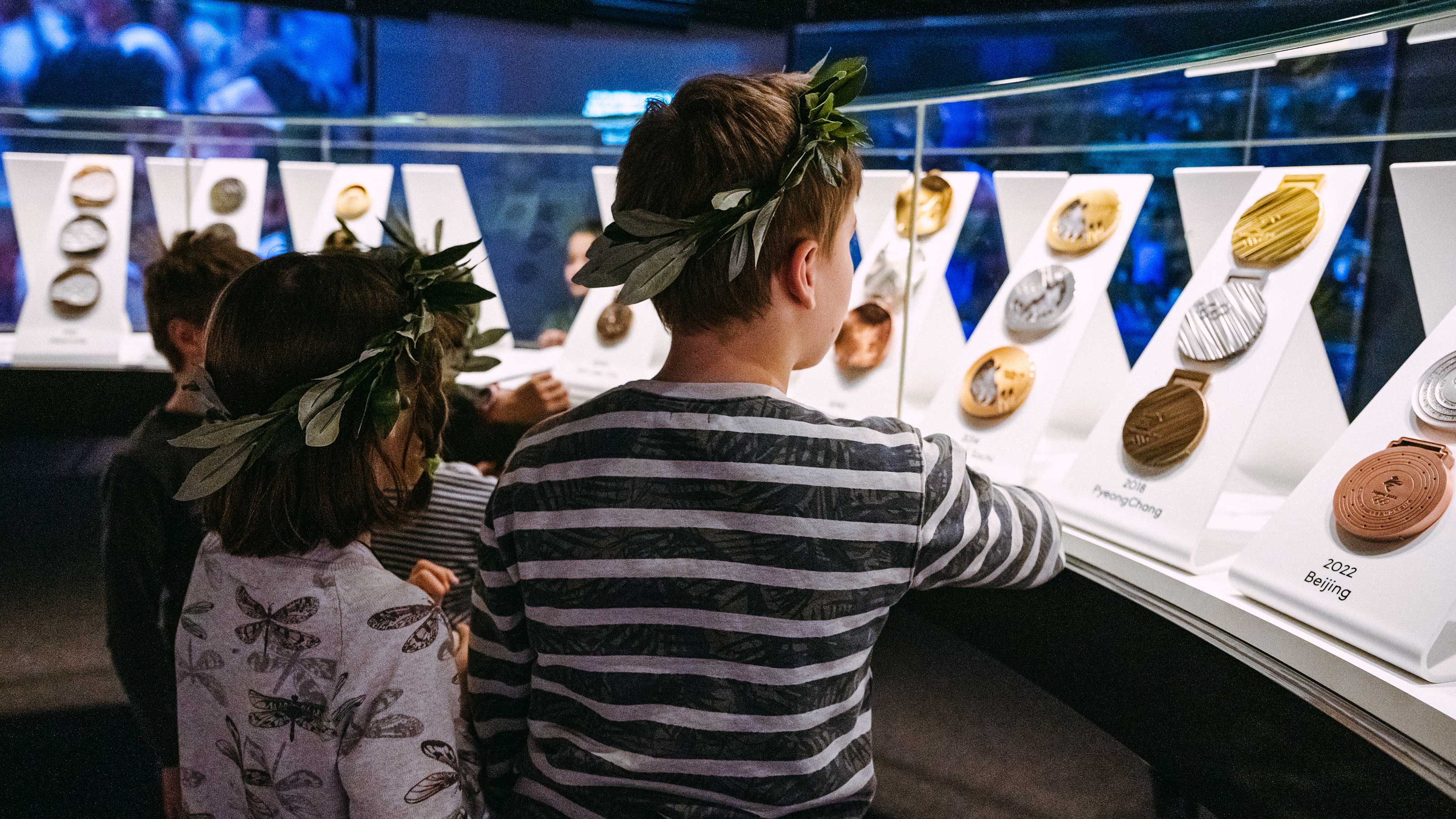 Deux enfants regardant une vitrine remplie de médailles brillantes, leurs visages illuminés par la curiosité et l'excitation.