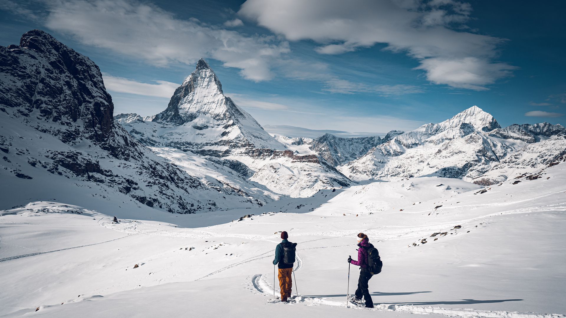 Ein Paar wandert mit Schneeschuhen durch eine verschneite Winterlandschaft mit dem imposanten Gipfel des Matterhorns im Blick.