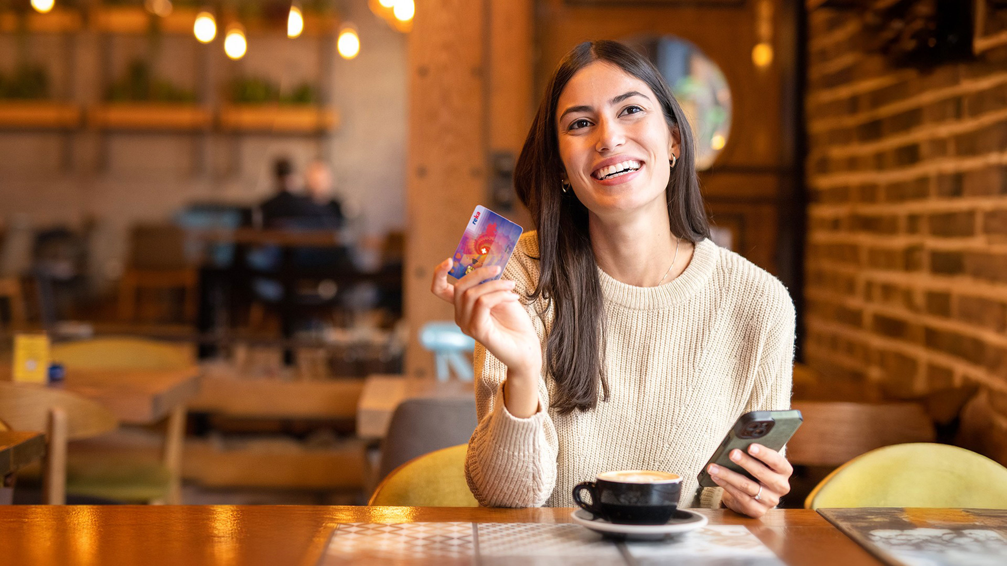 Una signora davanti a un tavolo con un caffè, il suo telefono pronto per pagare con la carta