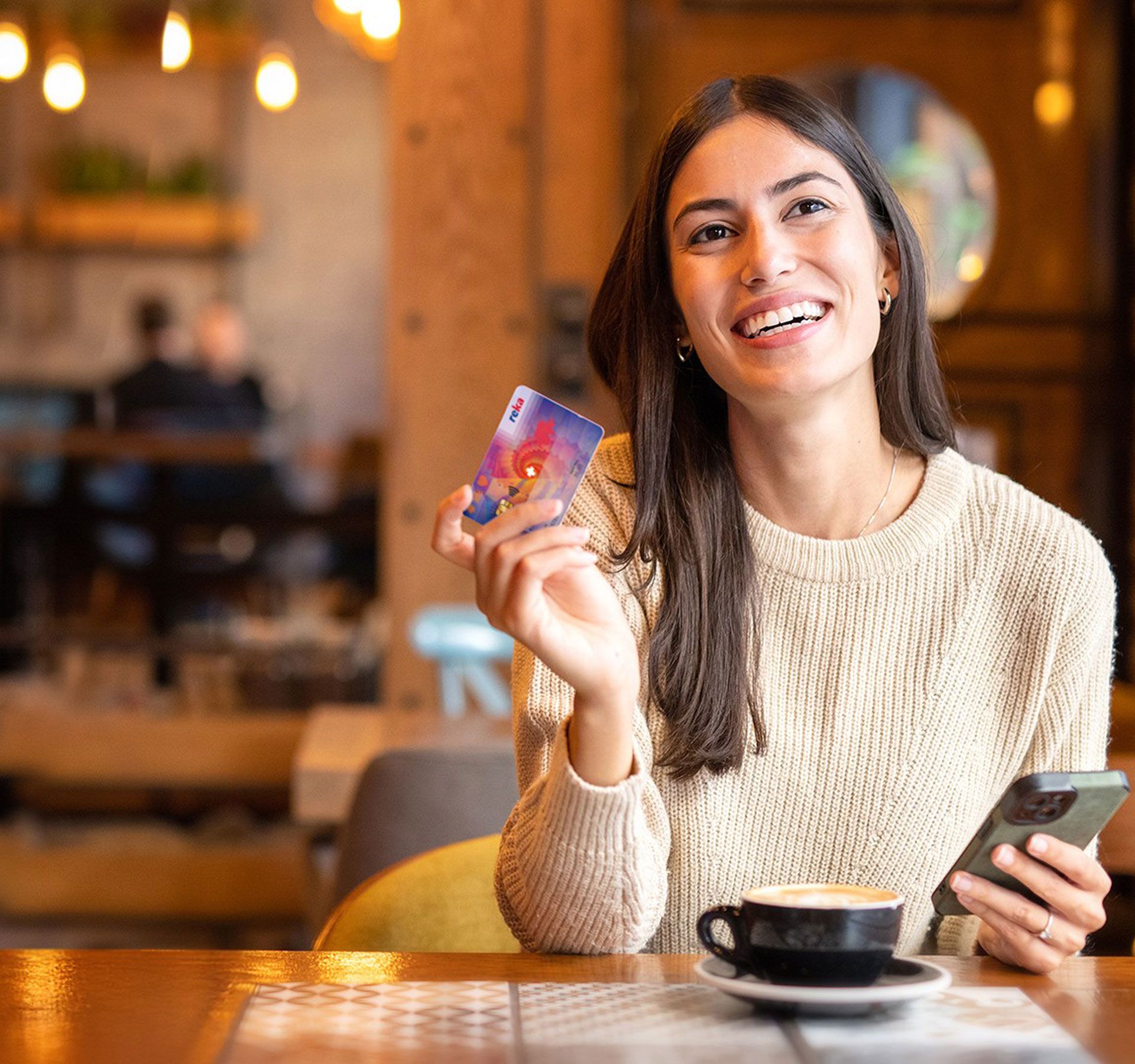 Una signora davanti a un tavolo con un caffè, il suo telefono pronto per pagare con la carta