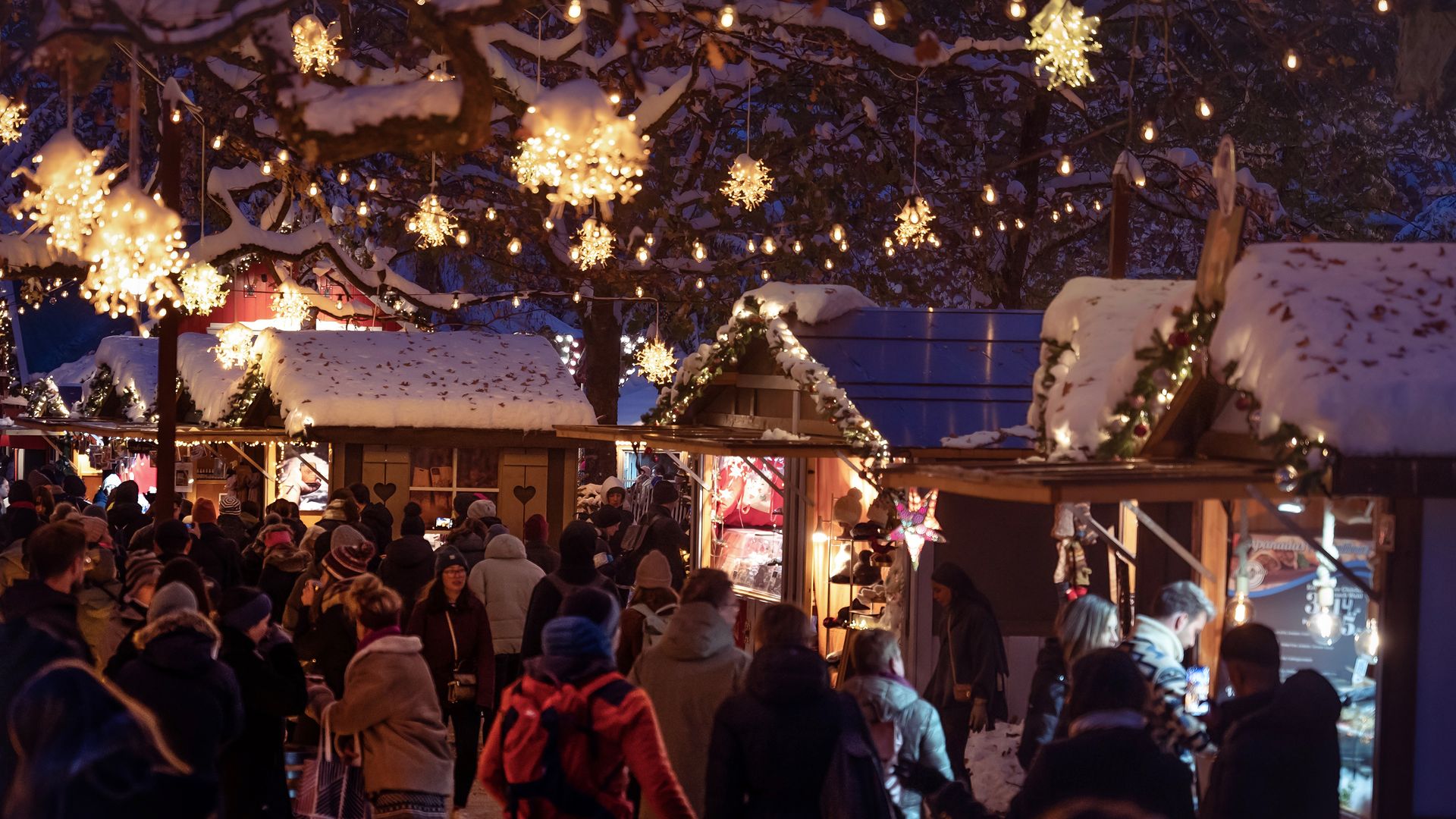 Menschen besuchen bei schöner Abendstimmung einen beleuchteten Weihnachtsmarkt.