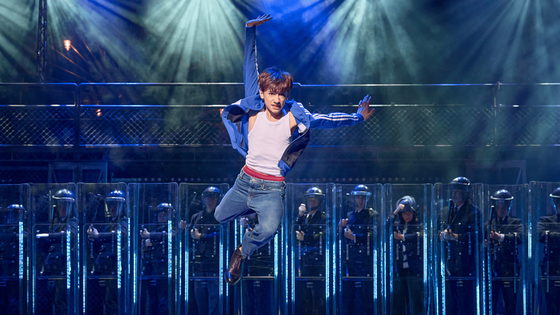 Un jeune danseur sur scène dans la comédie musicale « Billy Elliot », éclairé de façon expressive, avec une expression déterminée et une pose de danse.