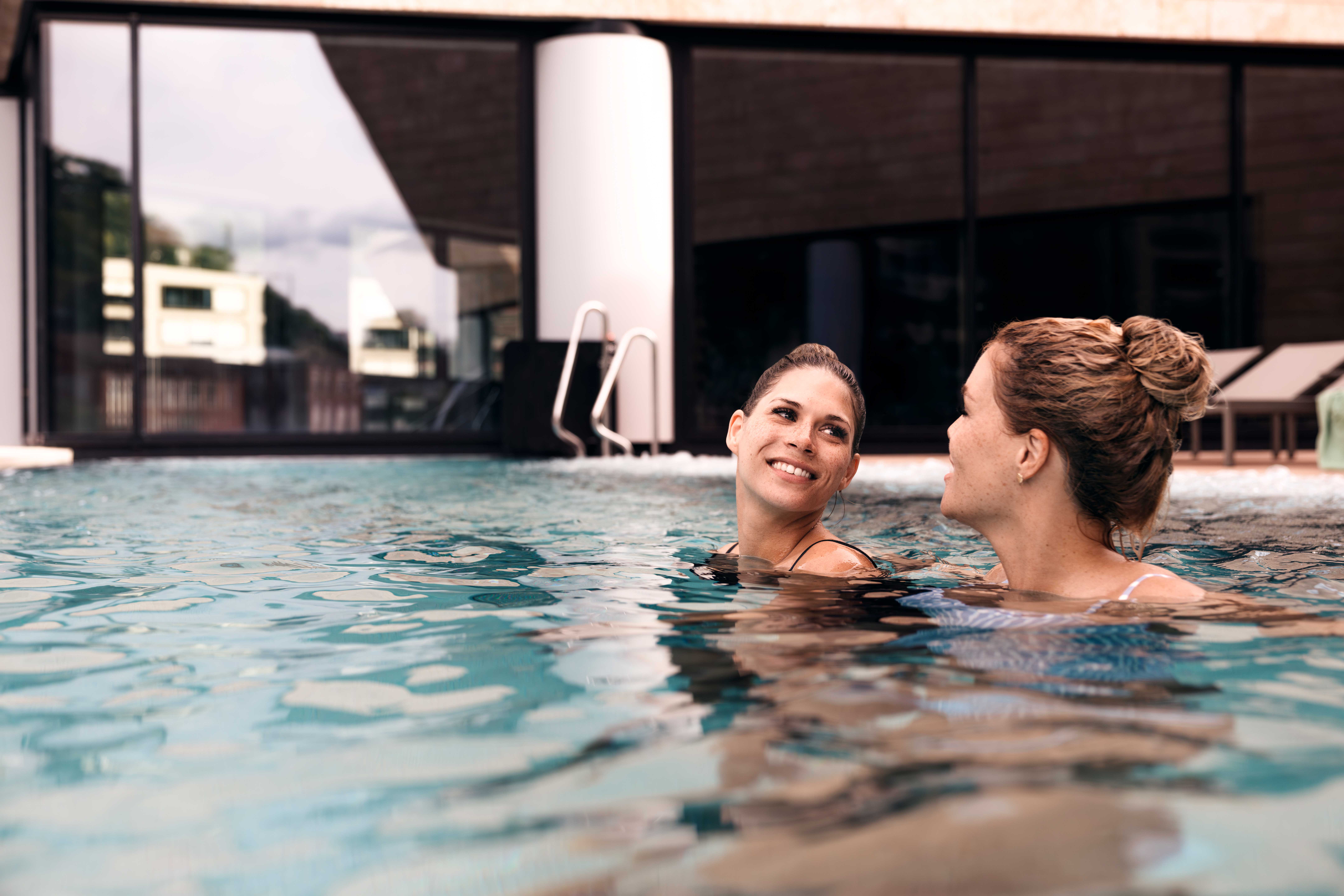 Due donne si godono un momento di relax in piscina, circondate da acque limpide e da un'atmosfera solare.