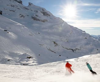 Zwei Personen fahren auf Skiern einen verschneiten Berg hinunter.