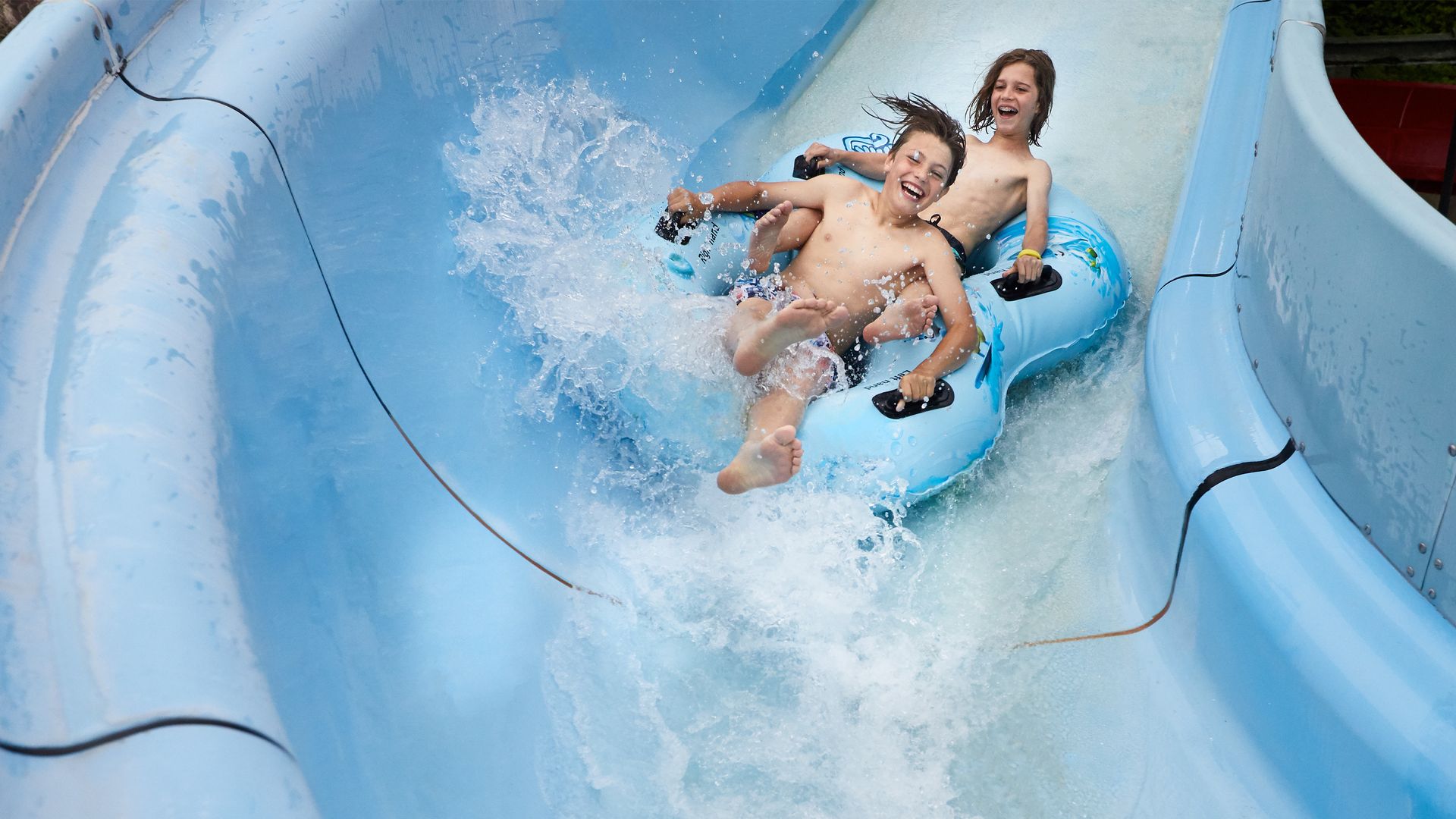 Deux joyeux enfants dévalent un toboggan aquatique sur un pneu gonflable.