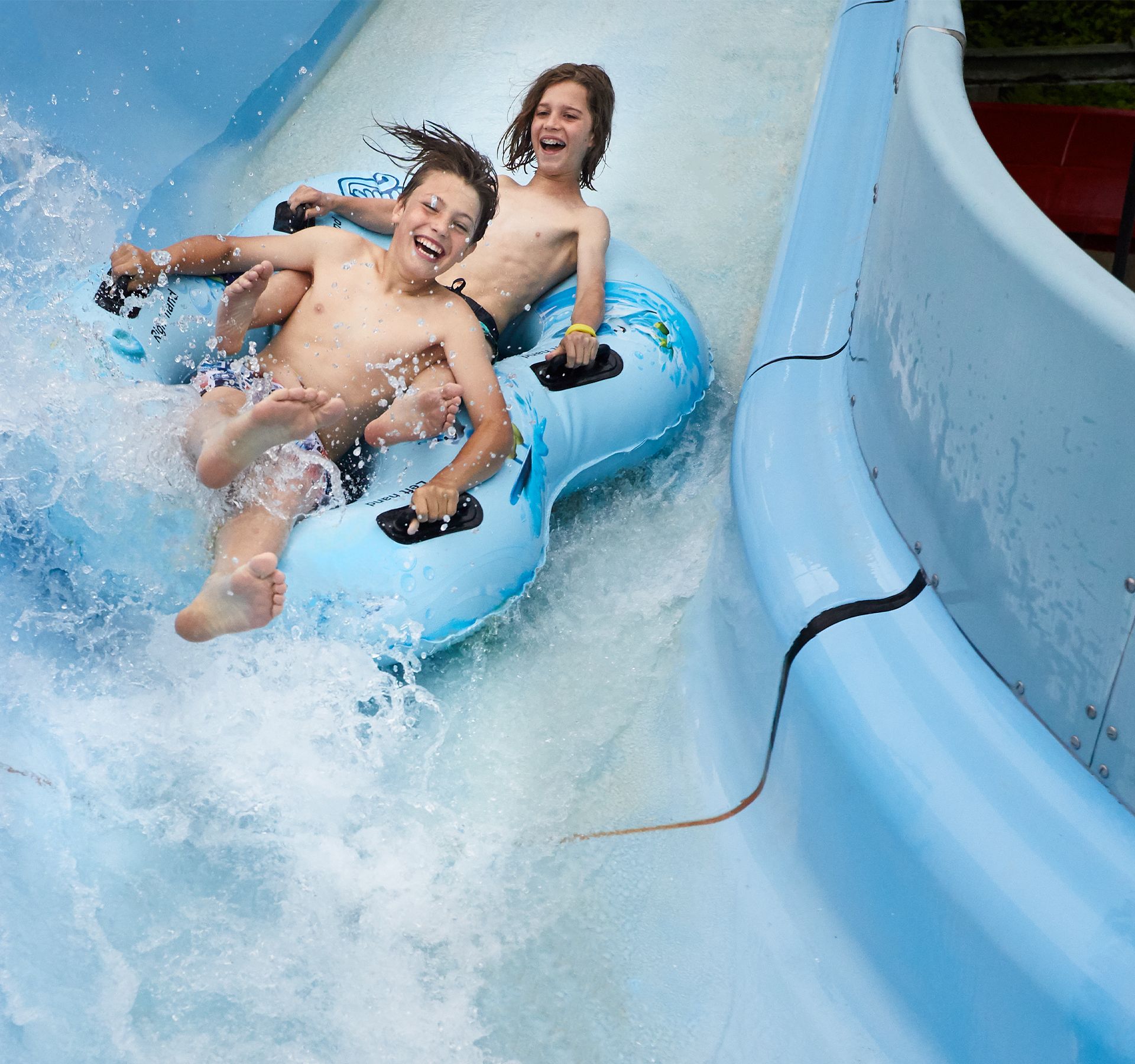 Due bambini felici scivolano lungo uno scivolo d'acqua su un pneumatico gonfiabile.