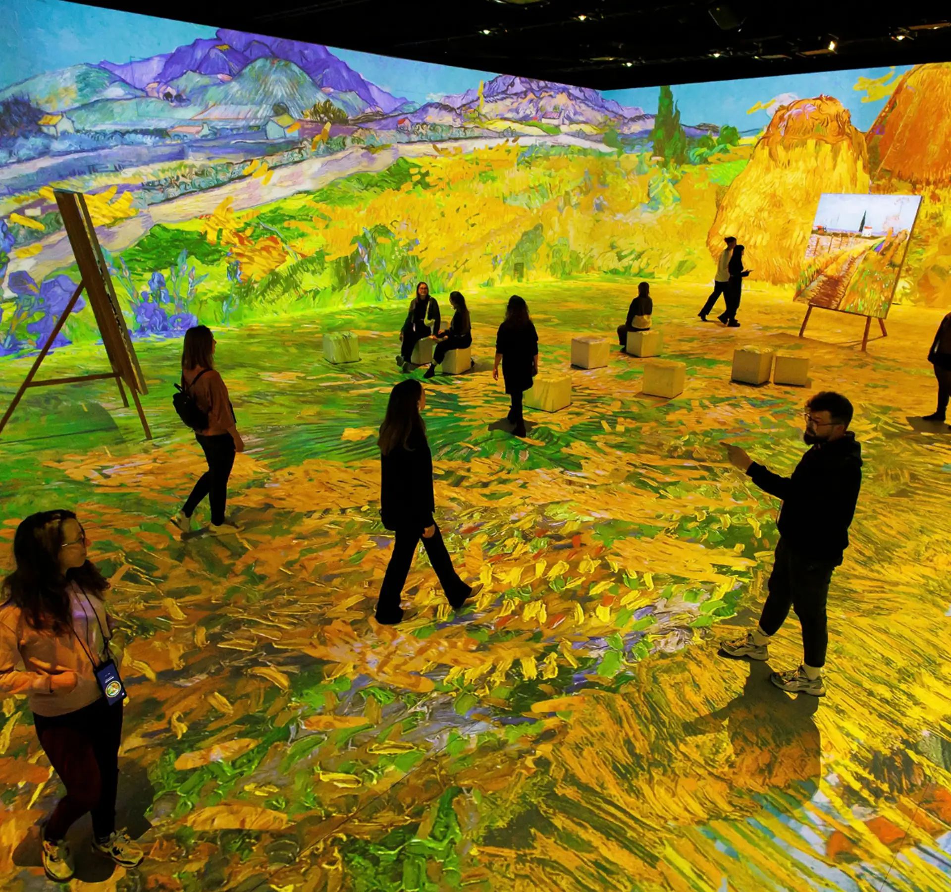 Several people walking in a room with large-scale projections of Vincent van Gogh paintings on walls and floor.