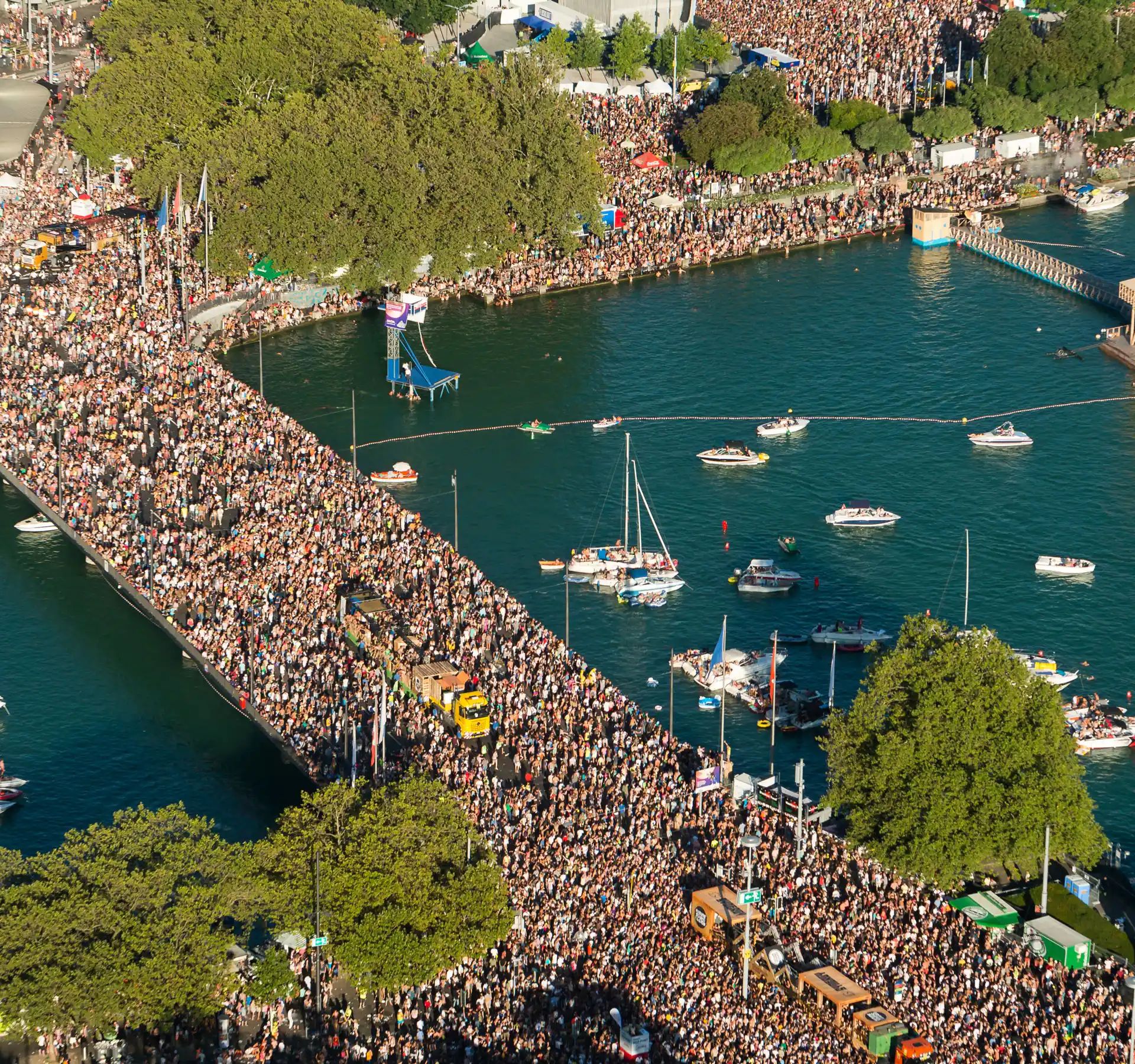 Luftaufnahme eines grossen Open-Air-Konzerts mit dicht gedrängtem Publikum vor einer Bühne am Flussufer.