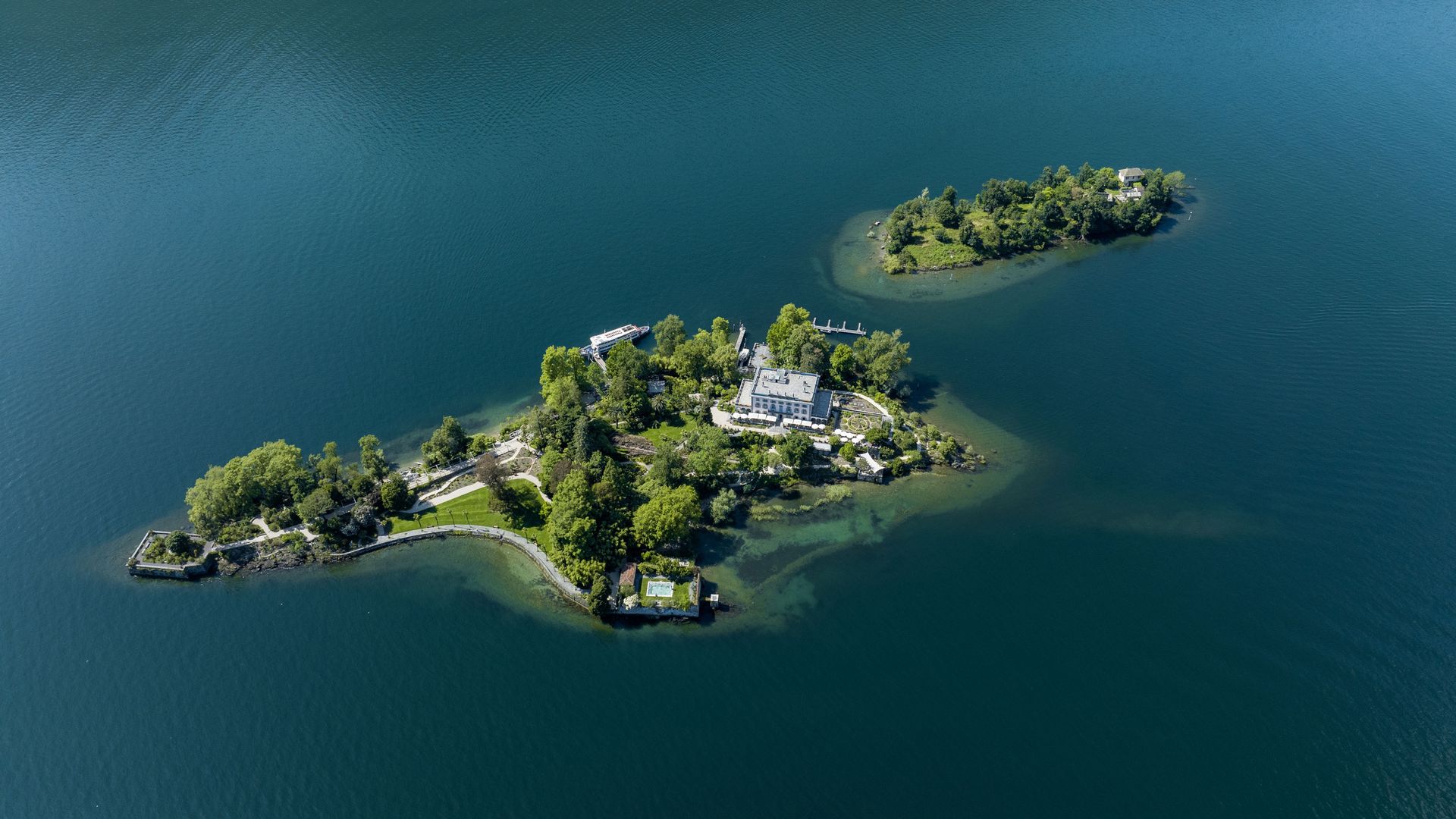 Un'isola soleggiata nel lago con una villa e una vegetazione verde.