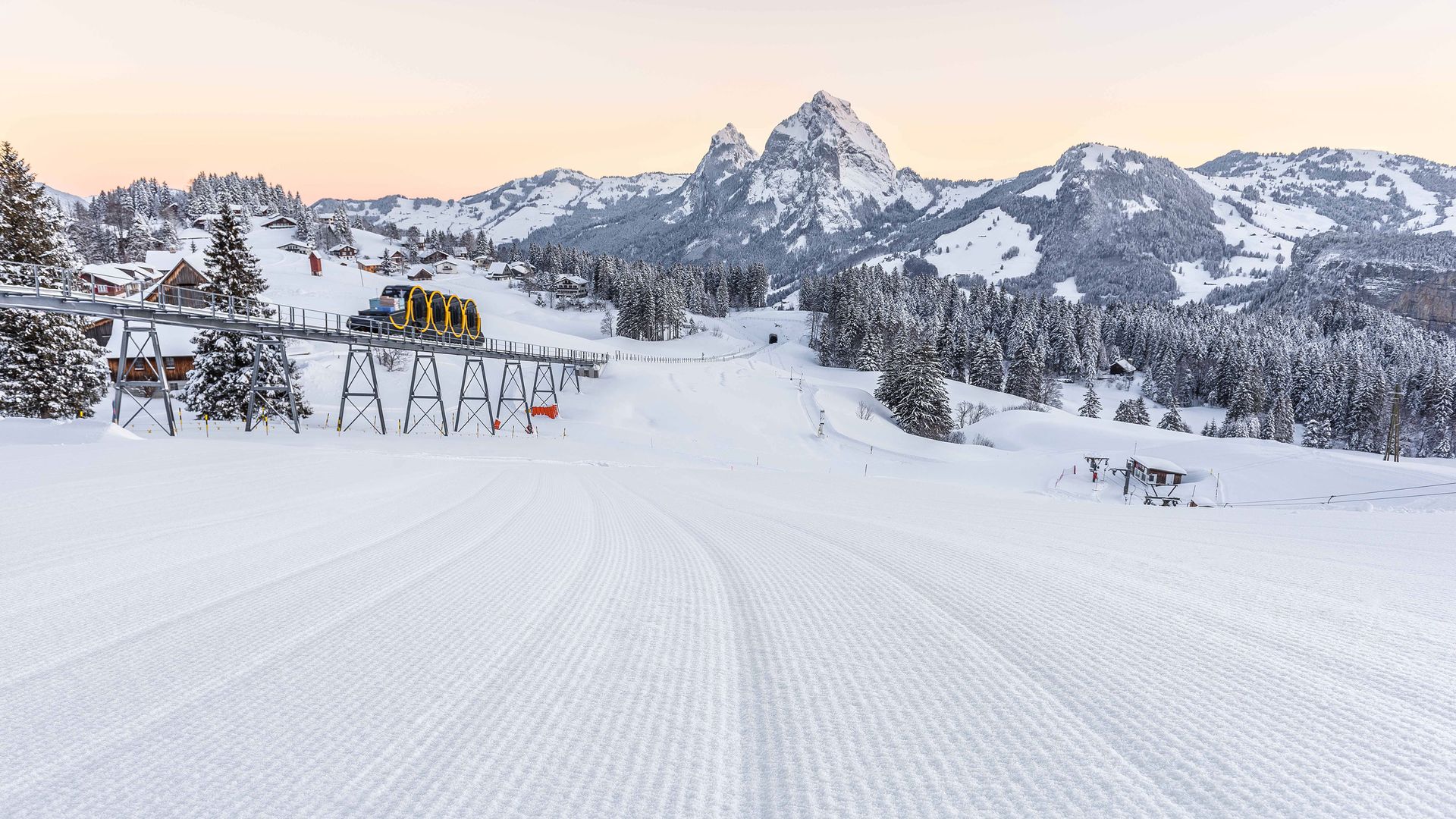Blick von der perfekt präparierten Piste auf die Standseilbahn und die umliegende Berglandschaft.