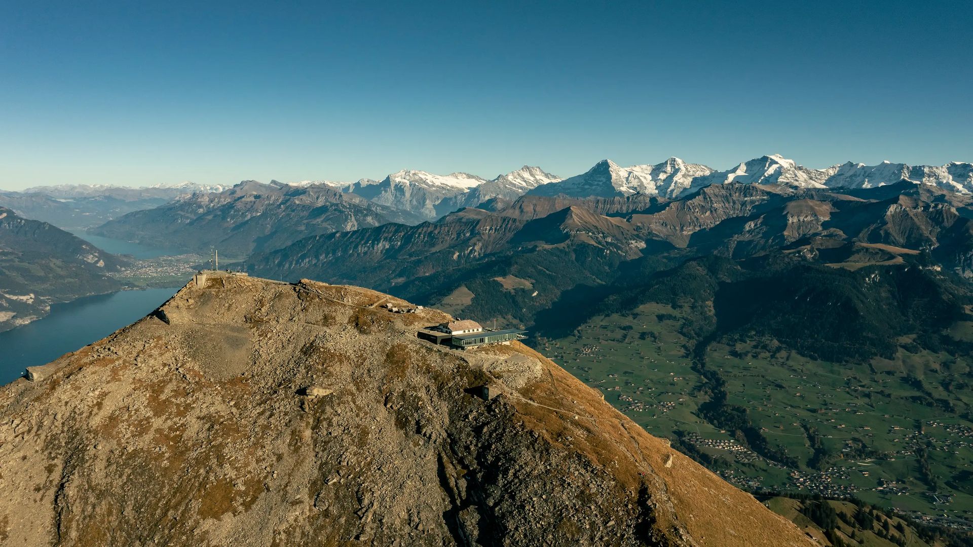 Aerial view of the Niesen mountain station on a rocky peak, with surrounding mountains and valleys in the background.