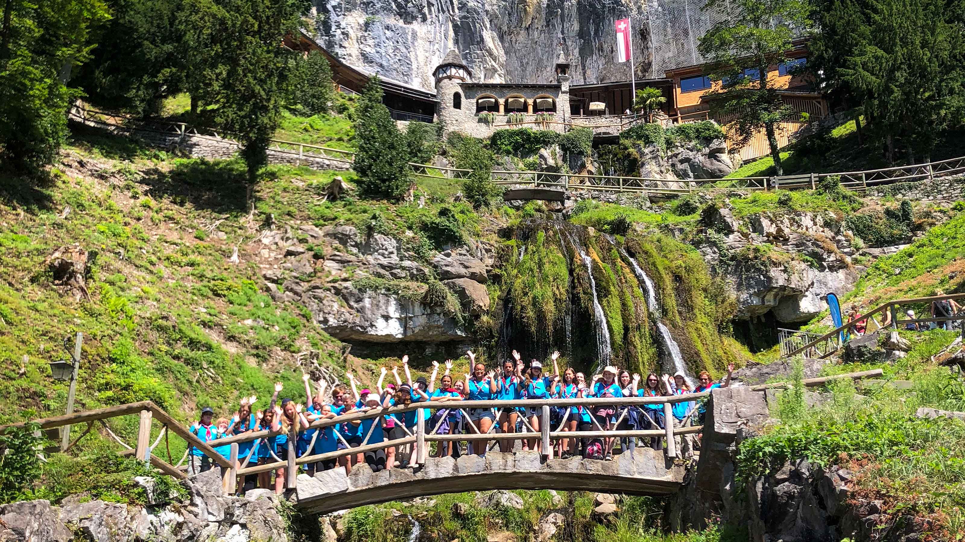 Una classe scolastica è in piedi su un ponte sotto l’ingresso delle grotte e alza le mani per la foto.