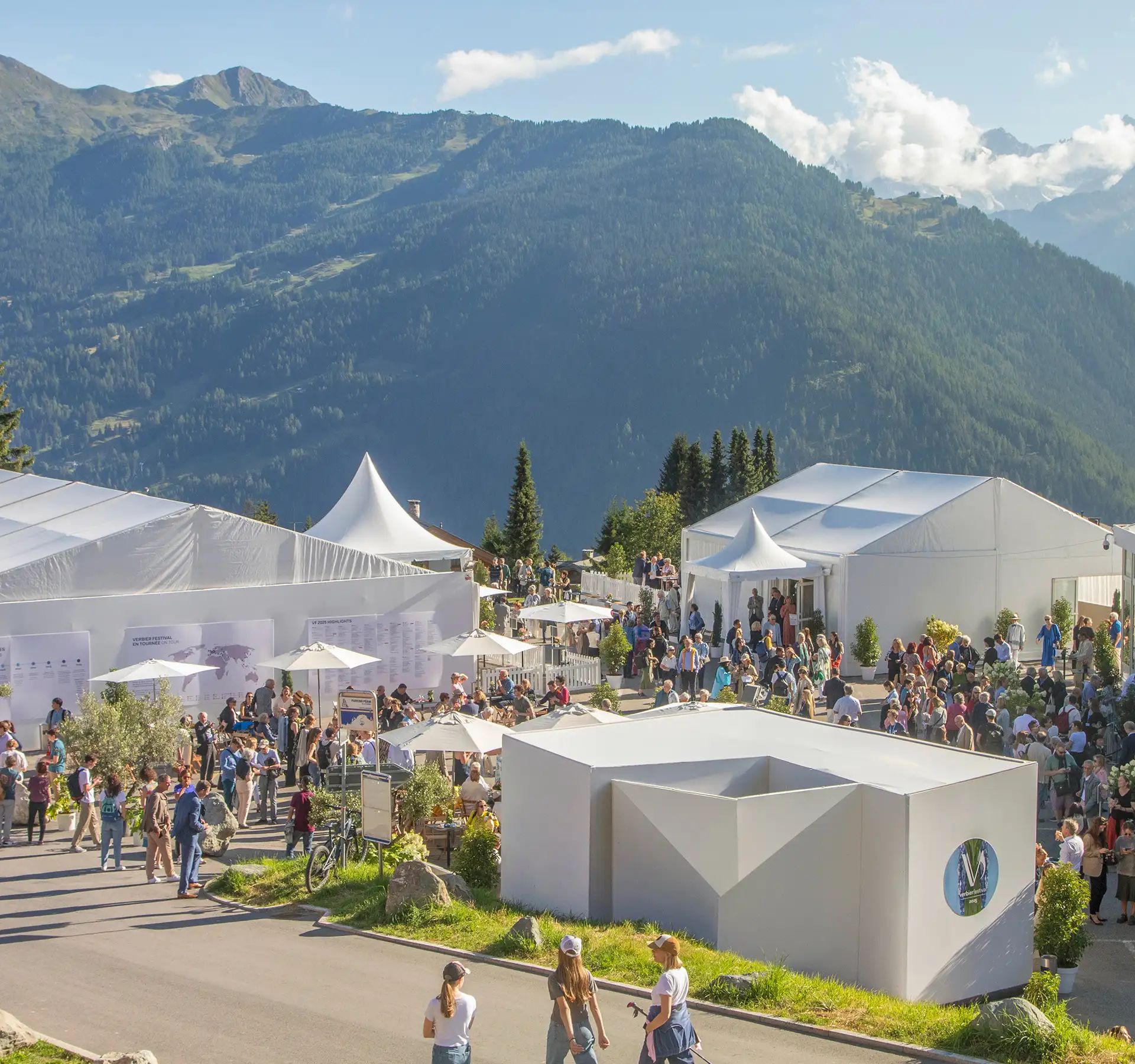 Crowd of people outside and inside a large white tent with the sign verbierfestival in a mountainous landscape.