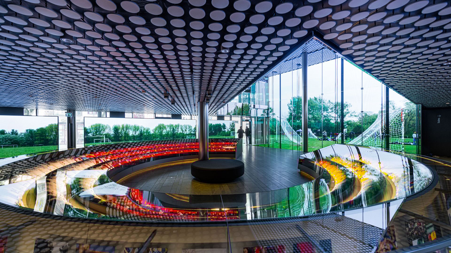 Vue intérieure du musée de la FIFA. Divers maillots de football sont exposés dans une très grande vitrine ronde. En arrière-plan, une grande baie vitrée donne sur une pelouse avec plusieurs buts de football.