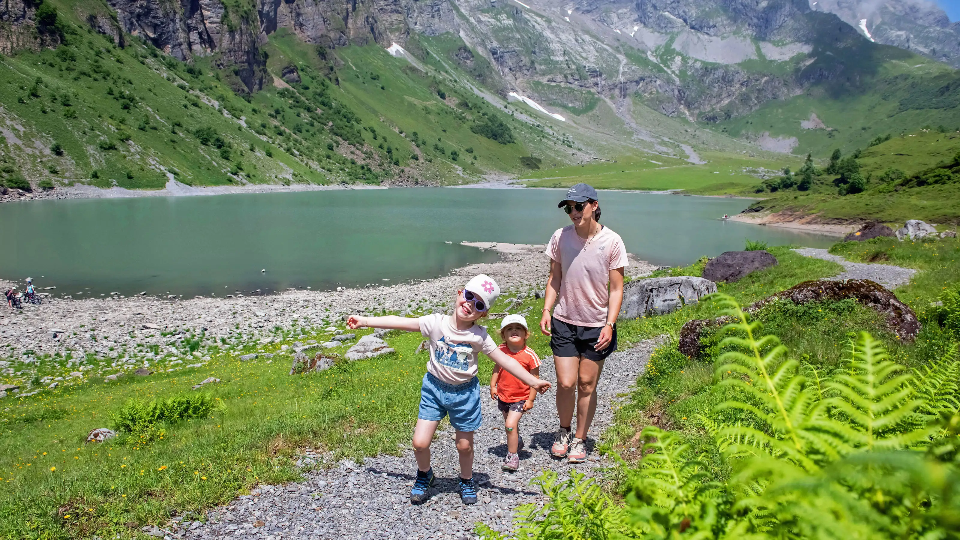  Zwei Kinder und eine Frau stehen auf einem Wanderweg am Oberblegisee, umgeben von grünen Wiesen und Bergen im Hintergrund