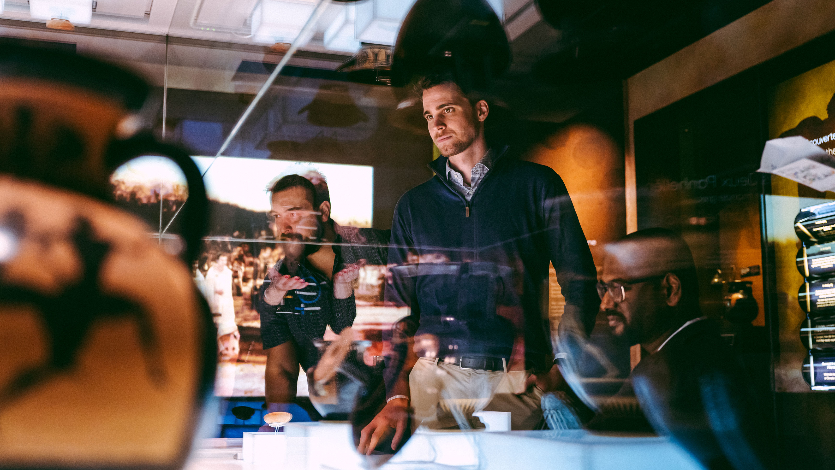  Several people look at exhibits behind a glass display case in an illuminated room in the Olympic Museum