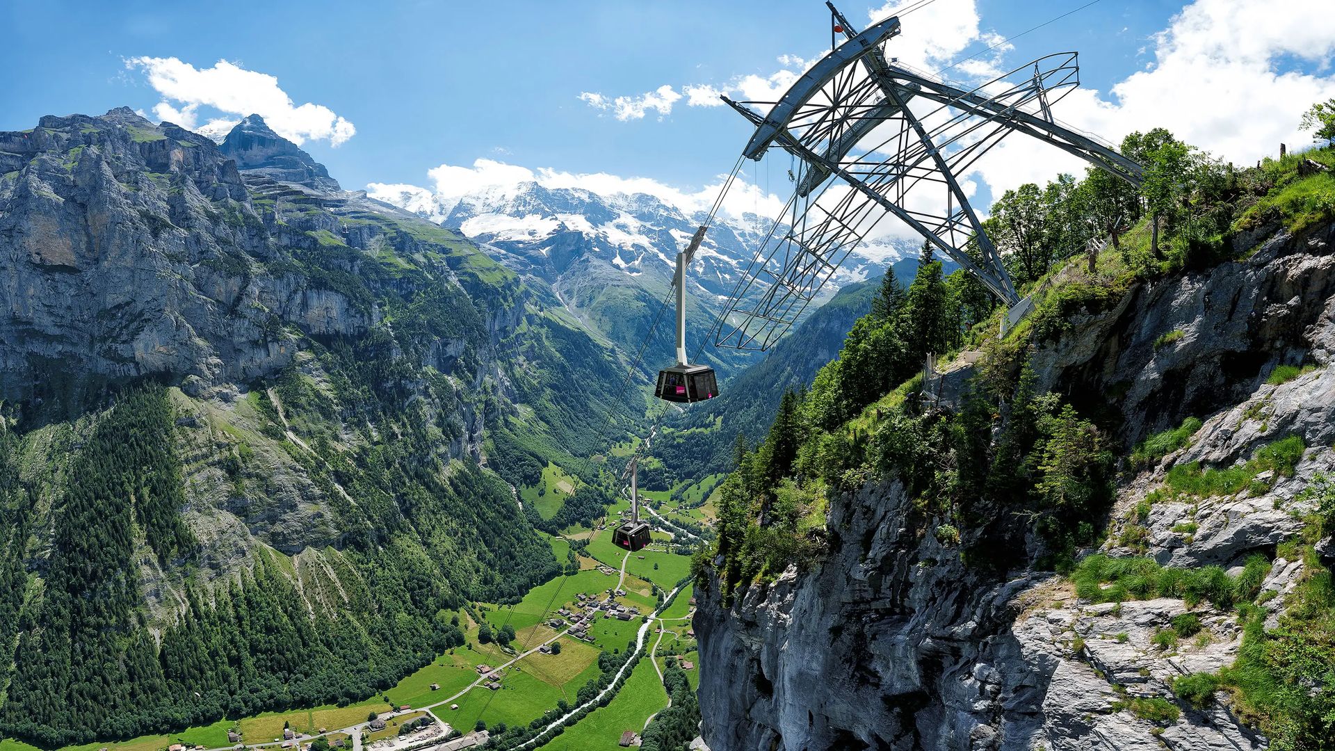 Schilthorn Seilbahn mit Gondeln an steiler Felswand über grünem Tal mit Berggipfeln im Hintergrund.