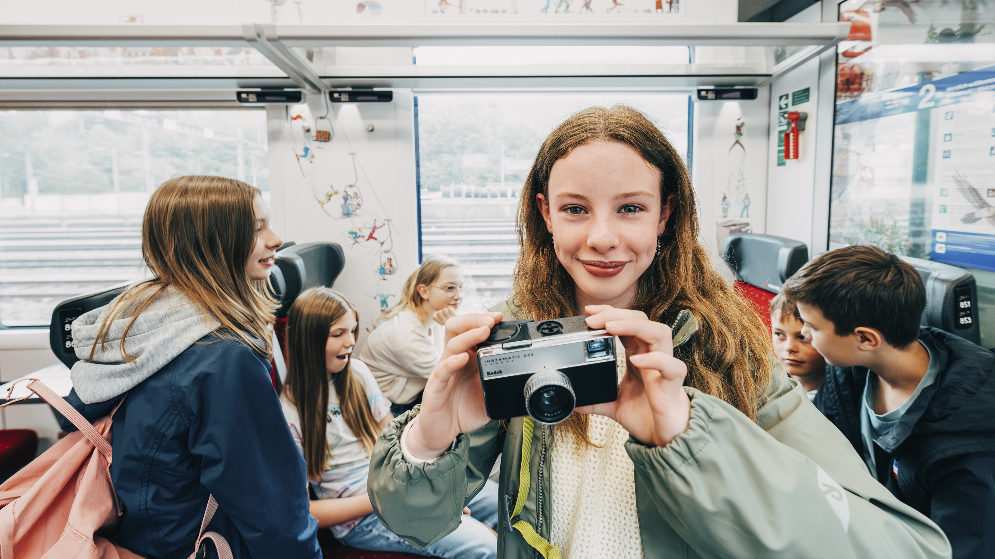 Ein Mädchen steht im Zugabteil und hält eine Kamera ins Bild.
