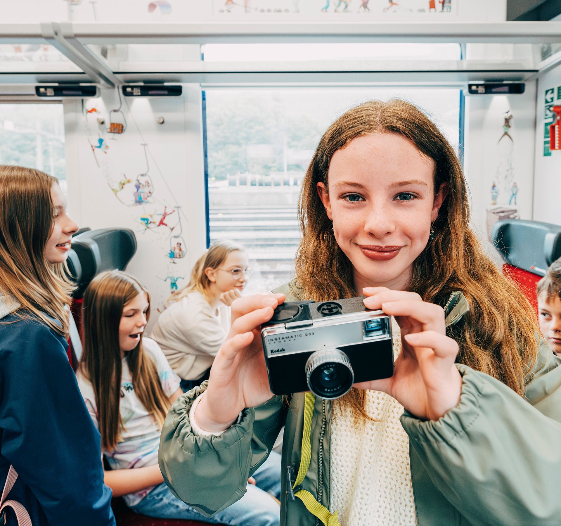 A girl stands in the train compartment and holds a camera into the picture.