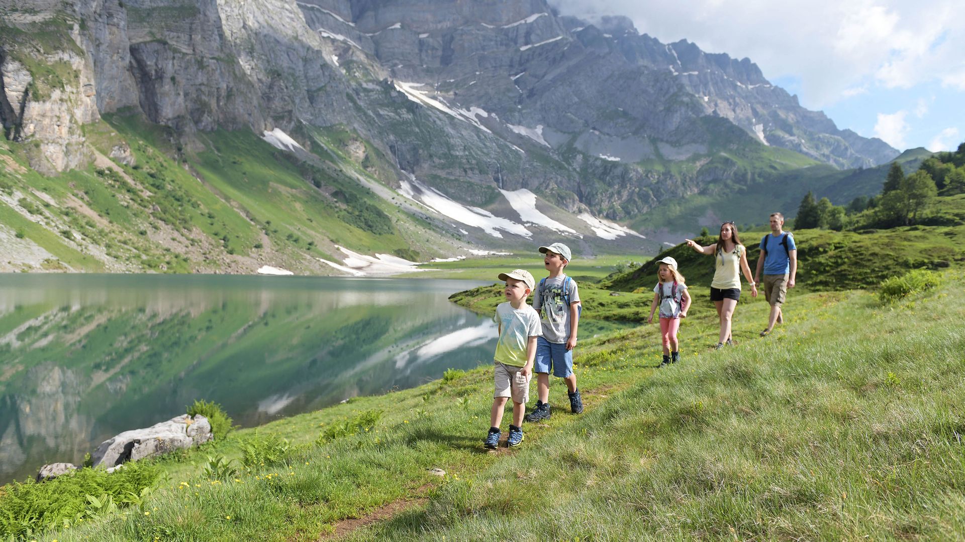 A family walks along the Oberblegisee on a mountain meadow.