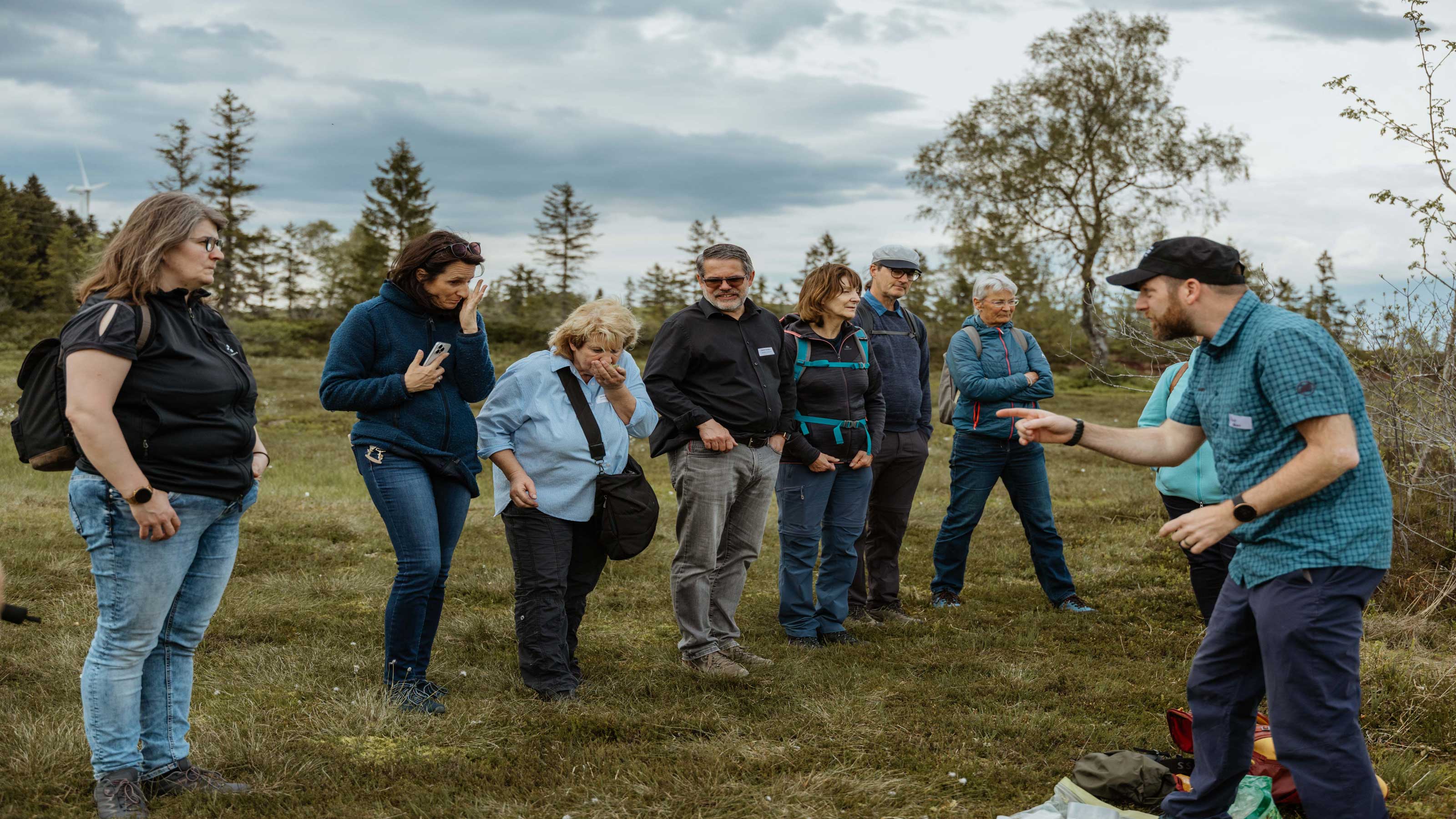 Un groupe de personnes se tient en plein air sur une tourbière. Un guide explique quelque chose au groupe.