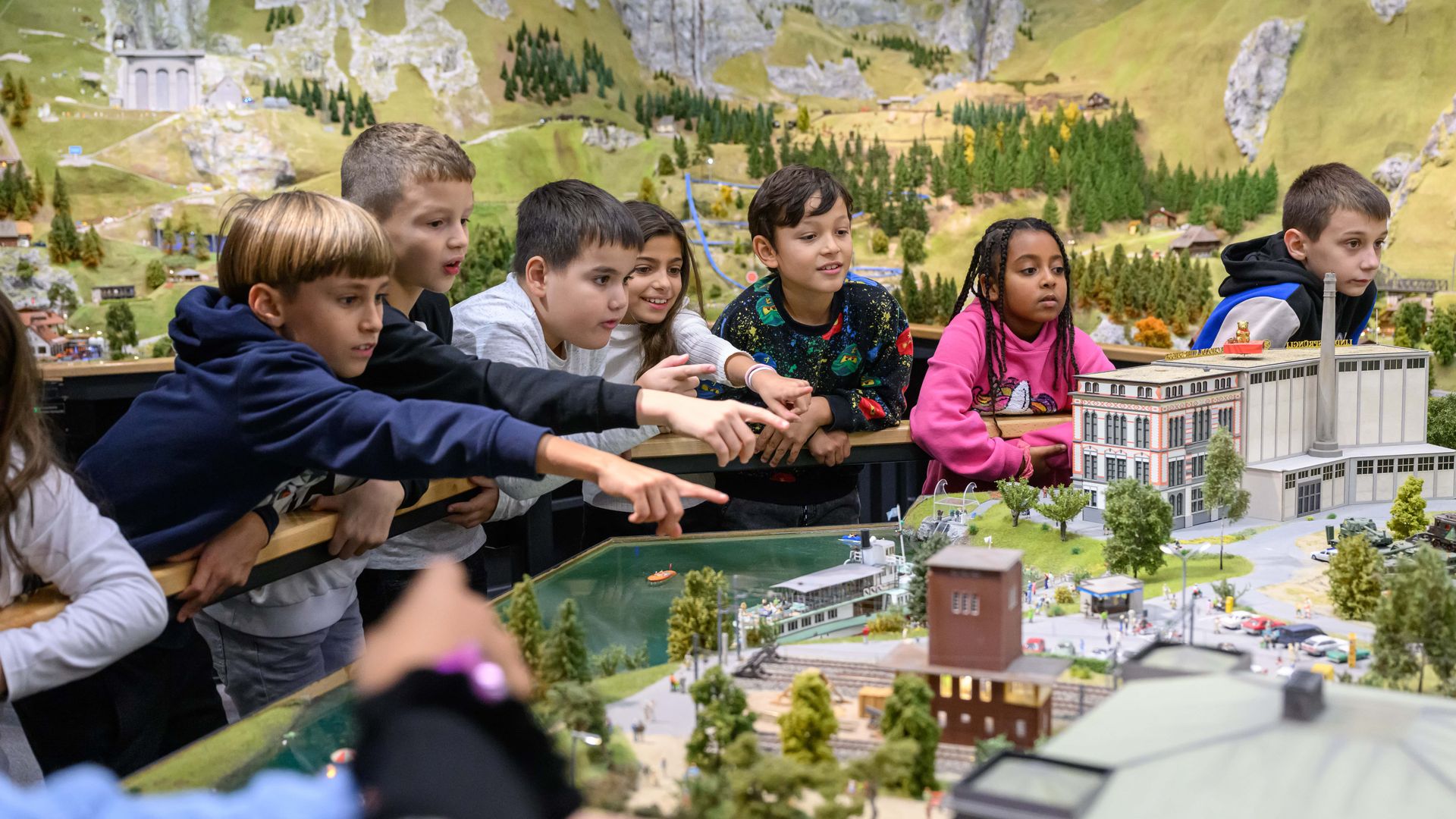 Un groupe d'enfants se tient au bord d'un monde miniature. Certains montrent des choses du doigt et d'autres regardent les petits objets avec attention.