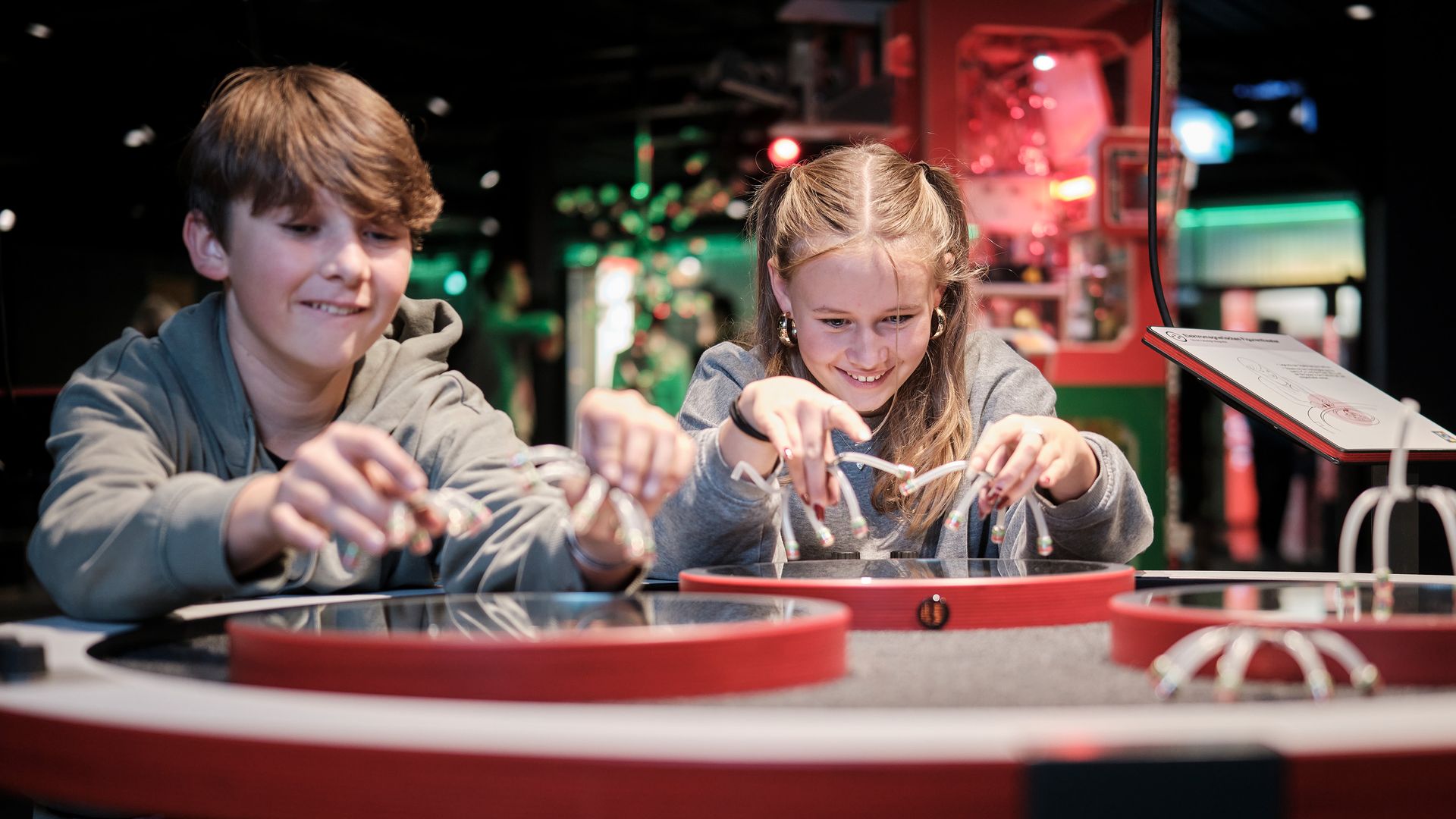 Zwei Kinder spielen freudig ein Spiel zusammen, umgeben von bunten Lichtern und lustigen Klängen in einem lebhaften Spielbereich.