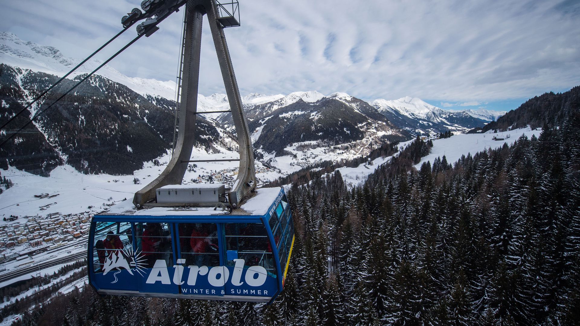 A cable car glides through snow-covered trees in a serene mountain landscape.