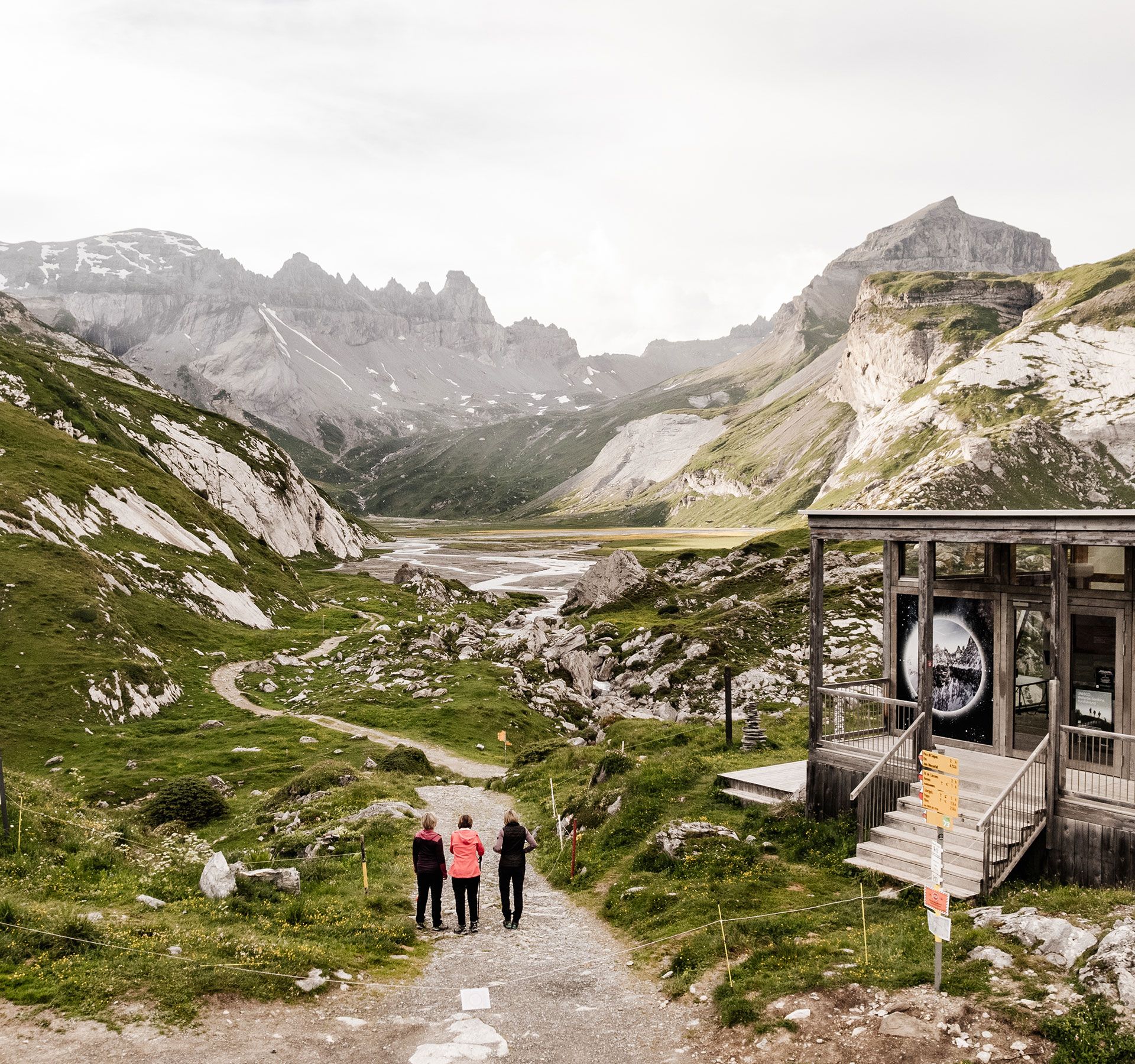 View of the UNESCO World Heritage Site Tectonic Arena Sardona in Switzerland: A group of three hikers stand on a path that leads through an impressive alpine landscape.