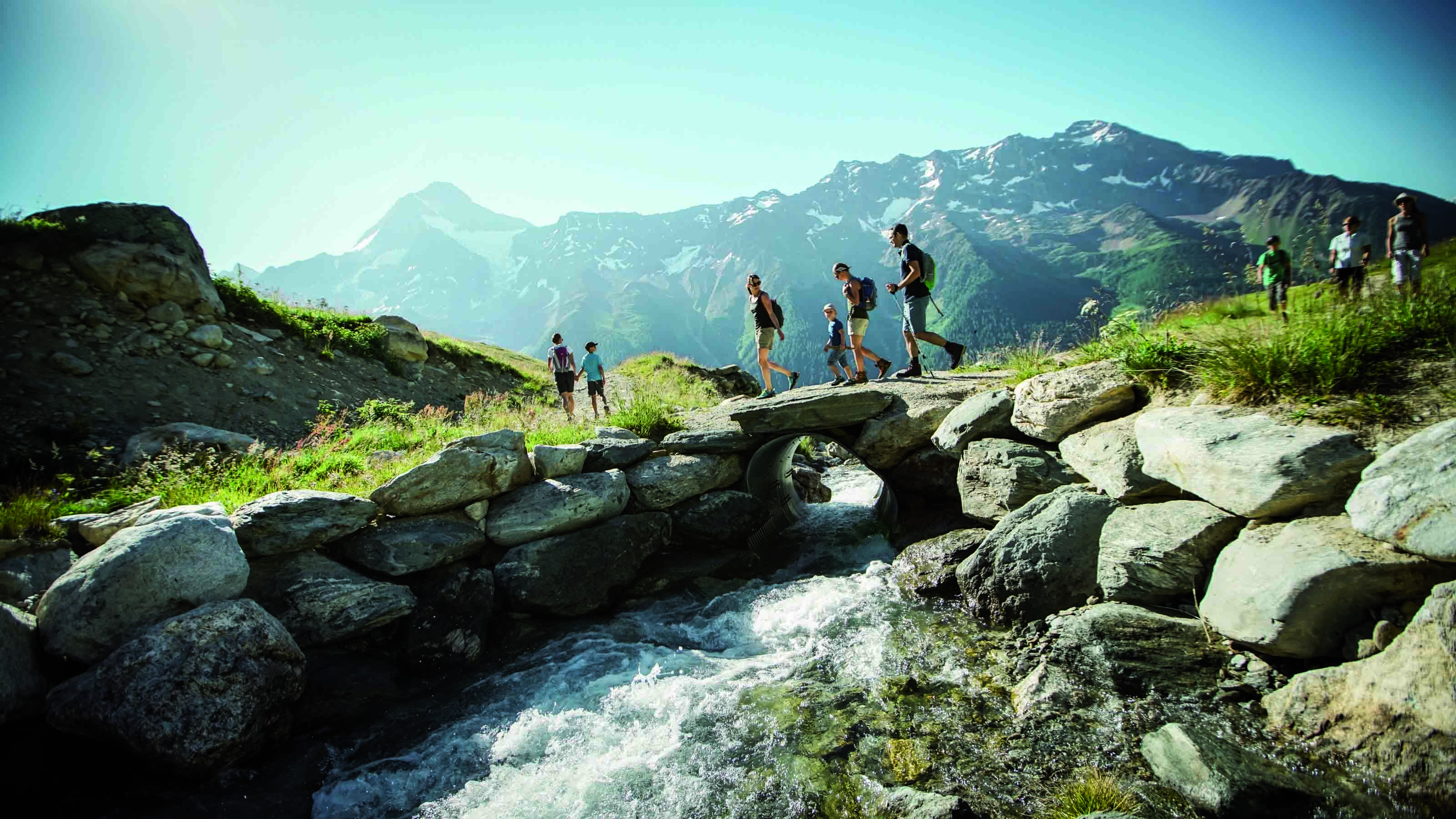 Una famiglia attraversa un piccolo ponte di pietra su un ruscello sul Lötschentaler Höhenweg.